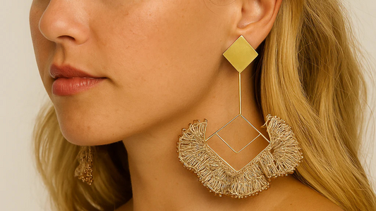 Close-up of a woman wearing a geometric gold earring with woven natural fringe detailing, styled with loose blonde waves.