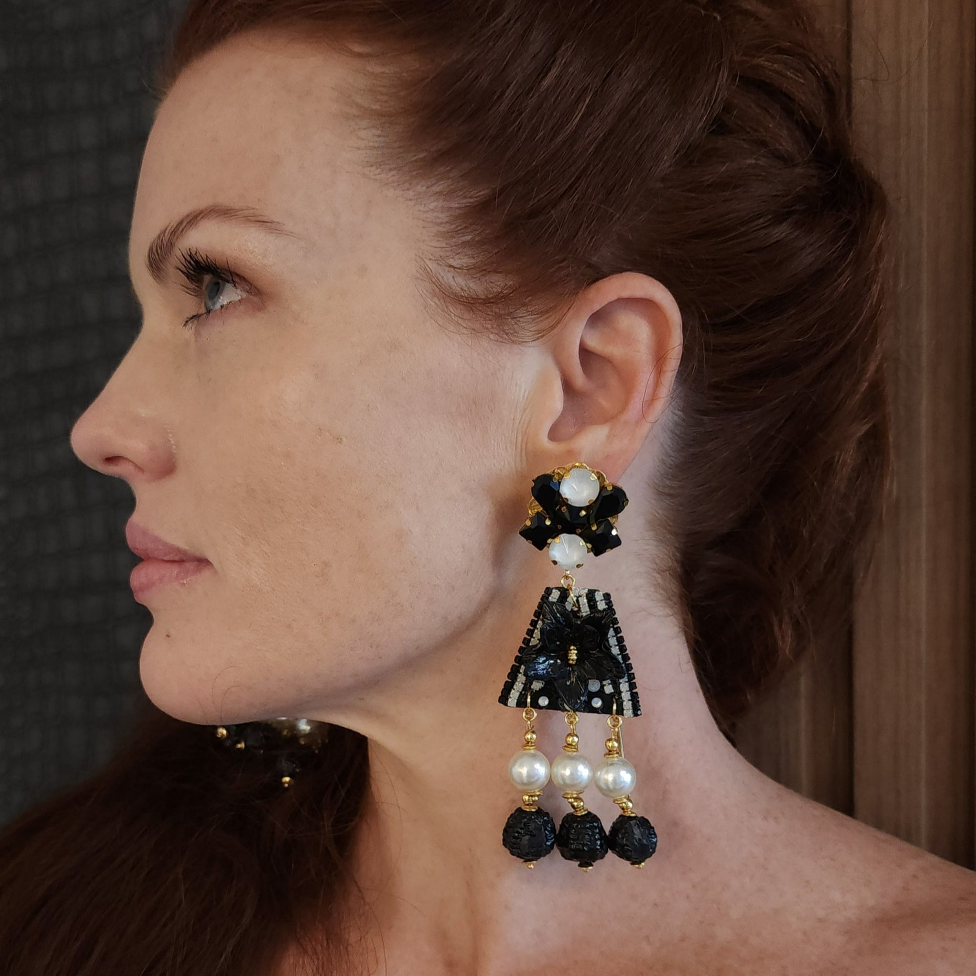 A close-up image of a woman wearing a black and white fiber triangle earring with day and night design, featuring pearls and black and white beads.