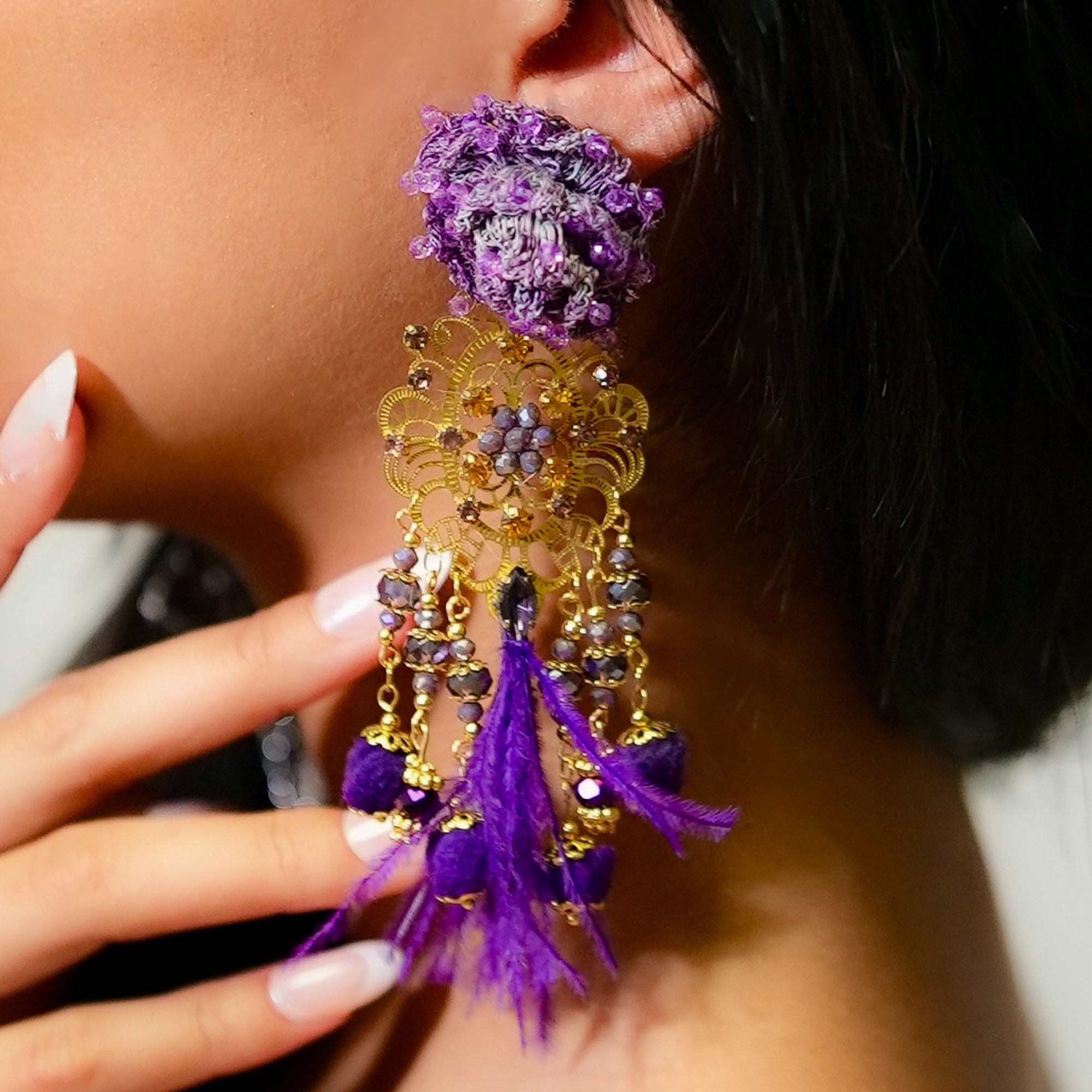 Close-up of a person wearing a purple and gold earring with feather details.