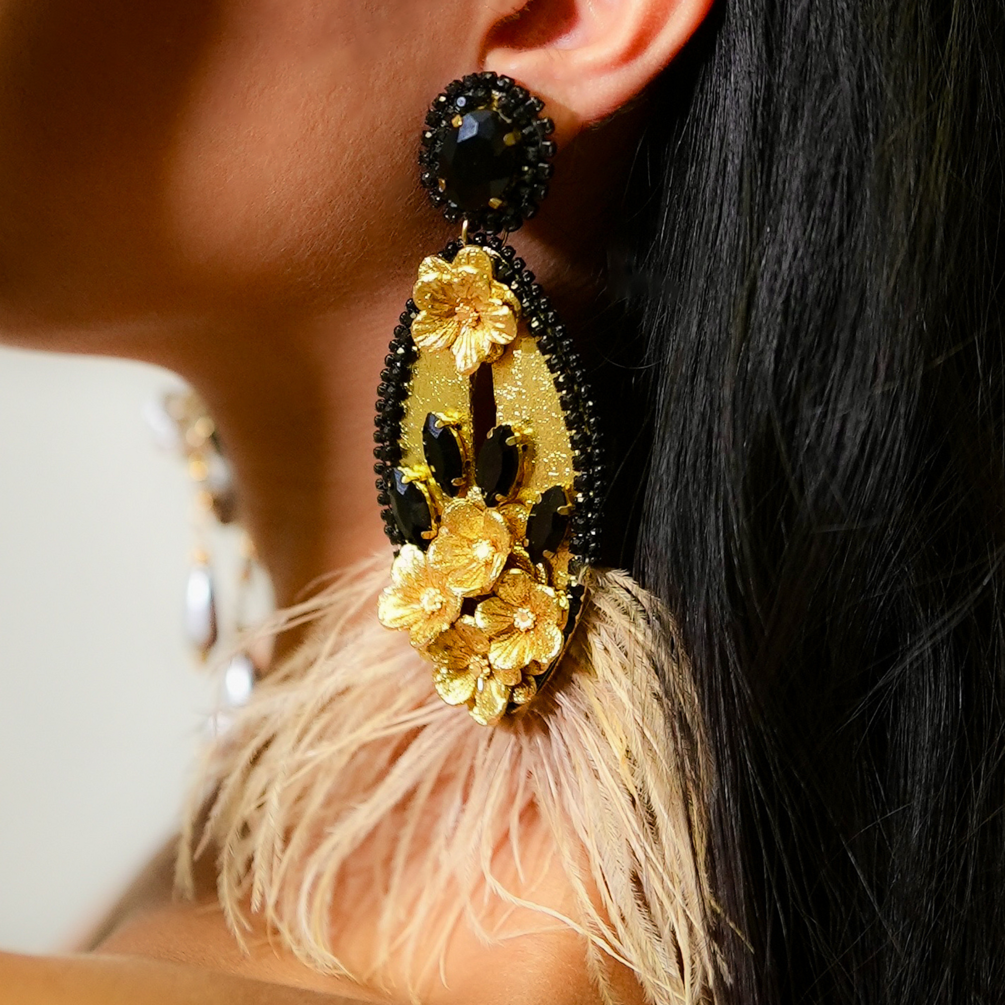 Close-up of a gold and black earring with feather details worn by a person.