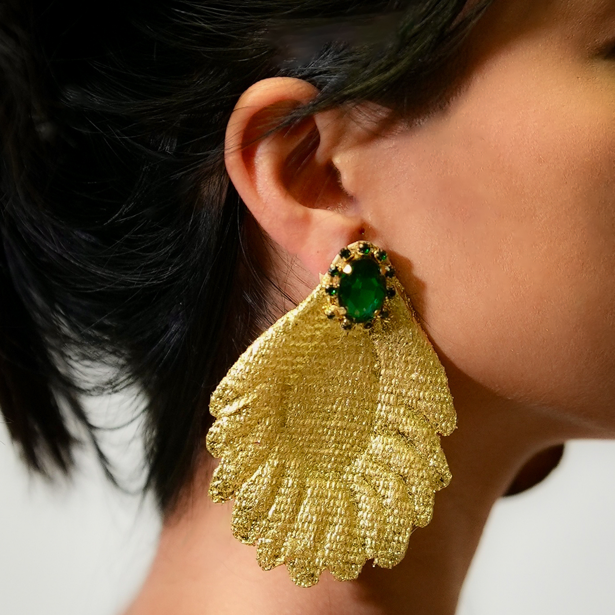 Gold earring with green gemstone worn by a person