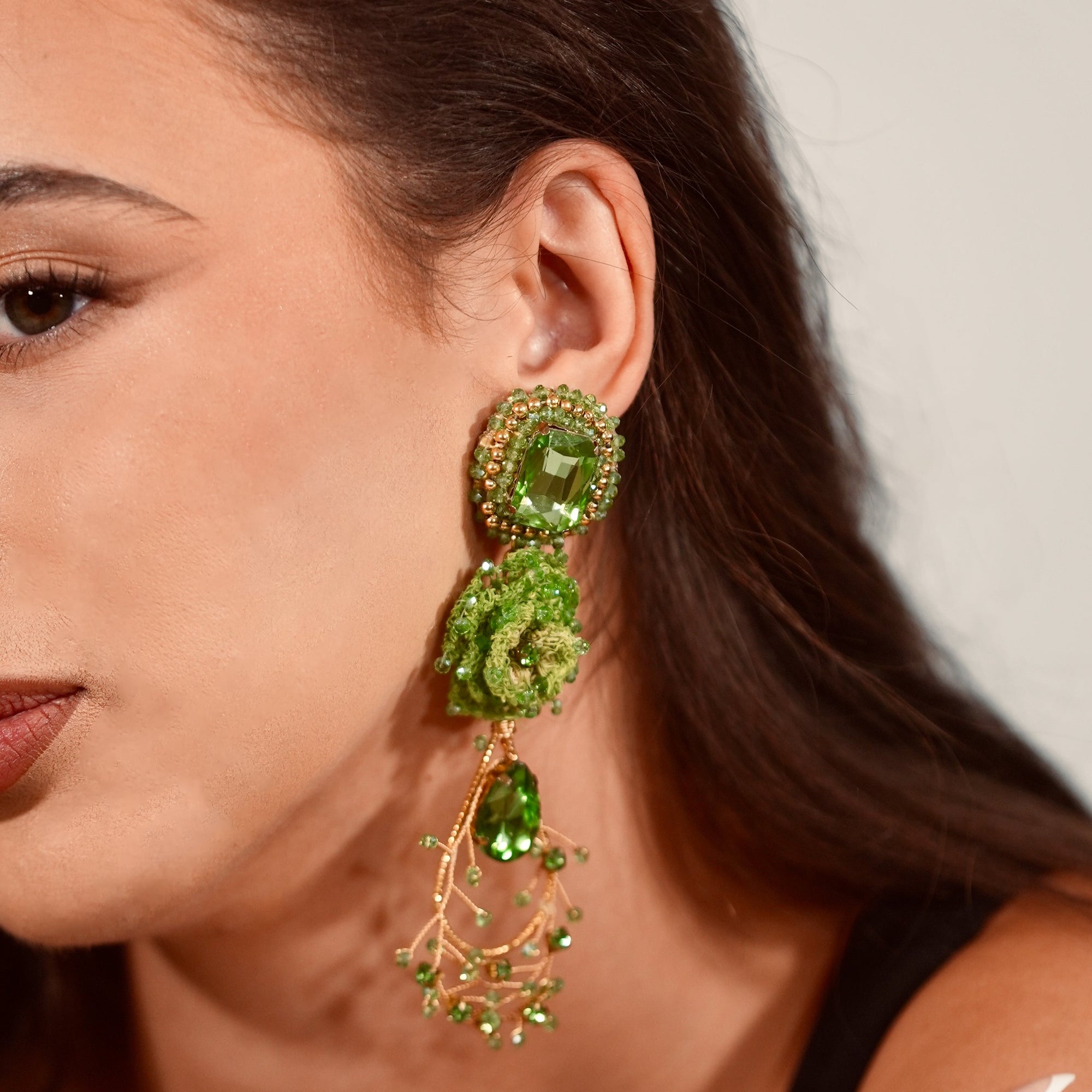 Close-up of a woman wearing green earrings with a neutral background