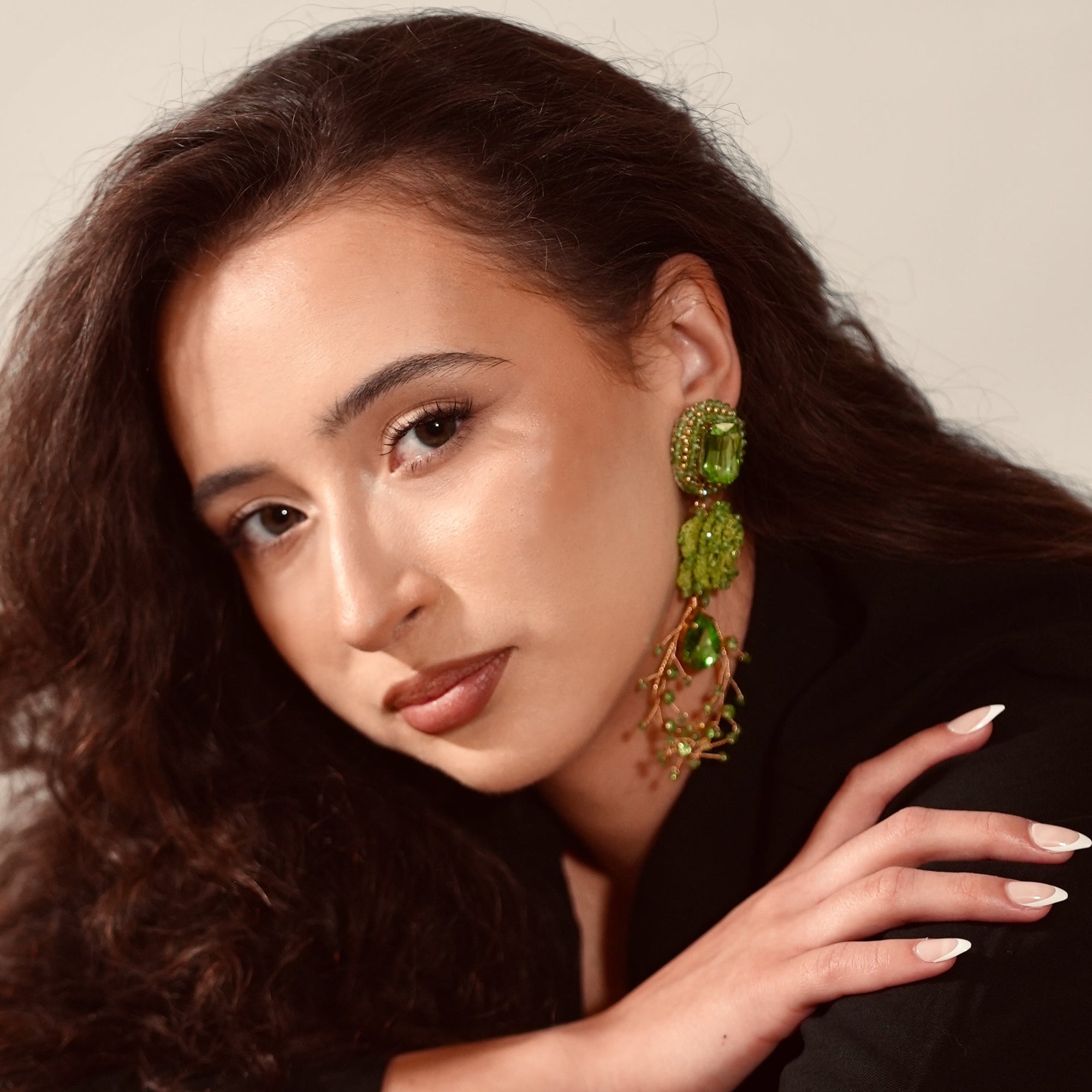 Woman wearing green earrings with a neutral background