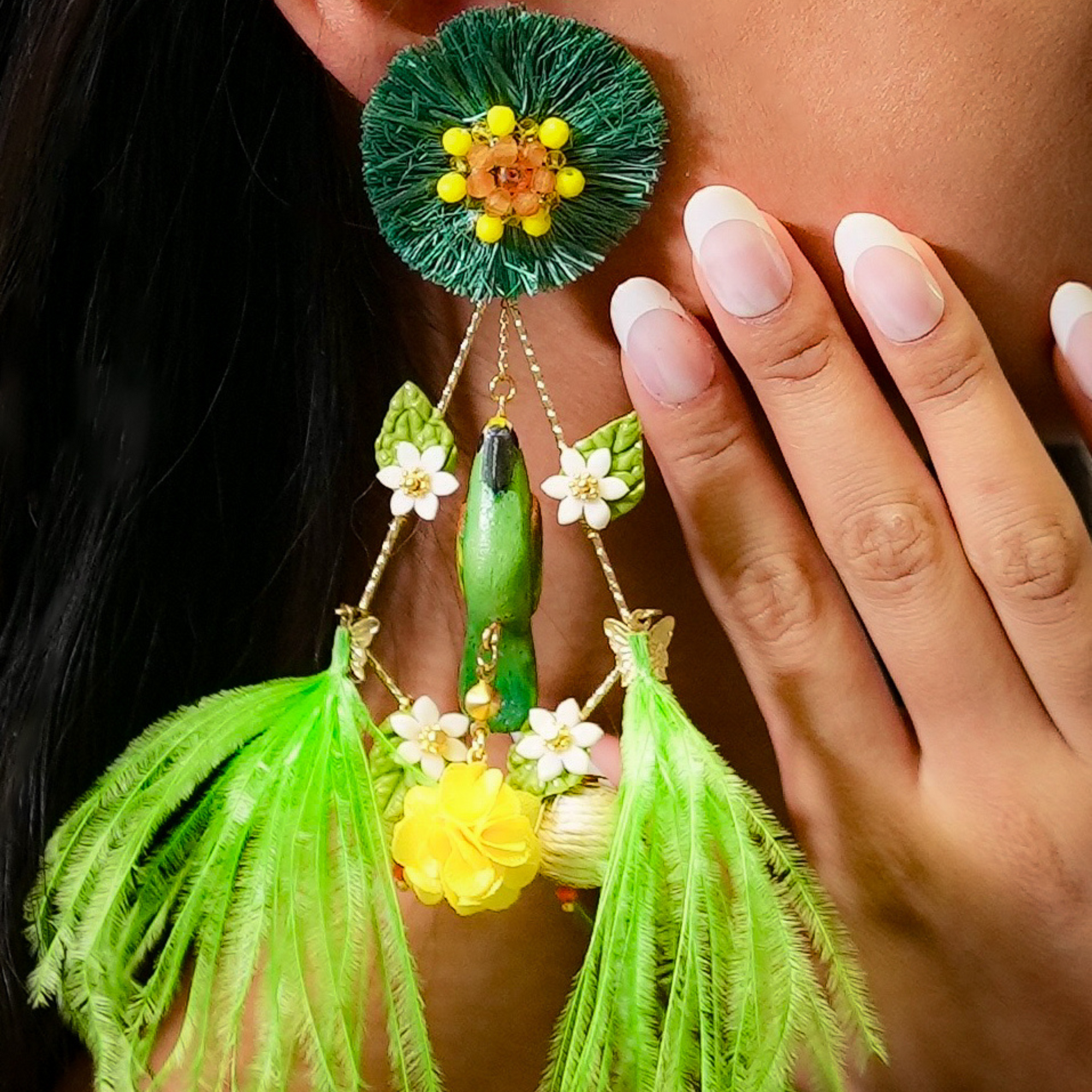 Close-up of a person wearing a pair of green and yellow earrings with floral and tassel details.