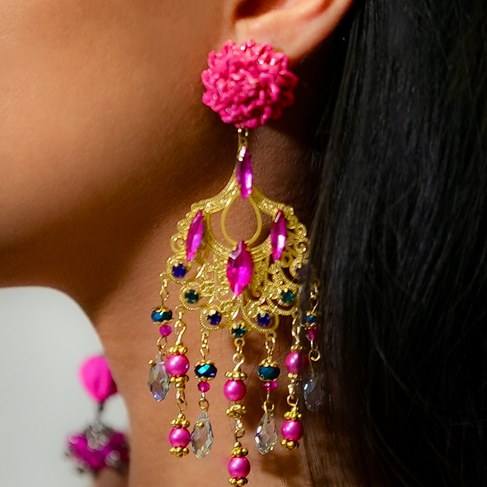 Close-up of a person wearing a colorful earring with pink flowers and gold accents.
