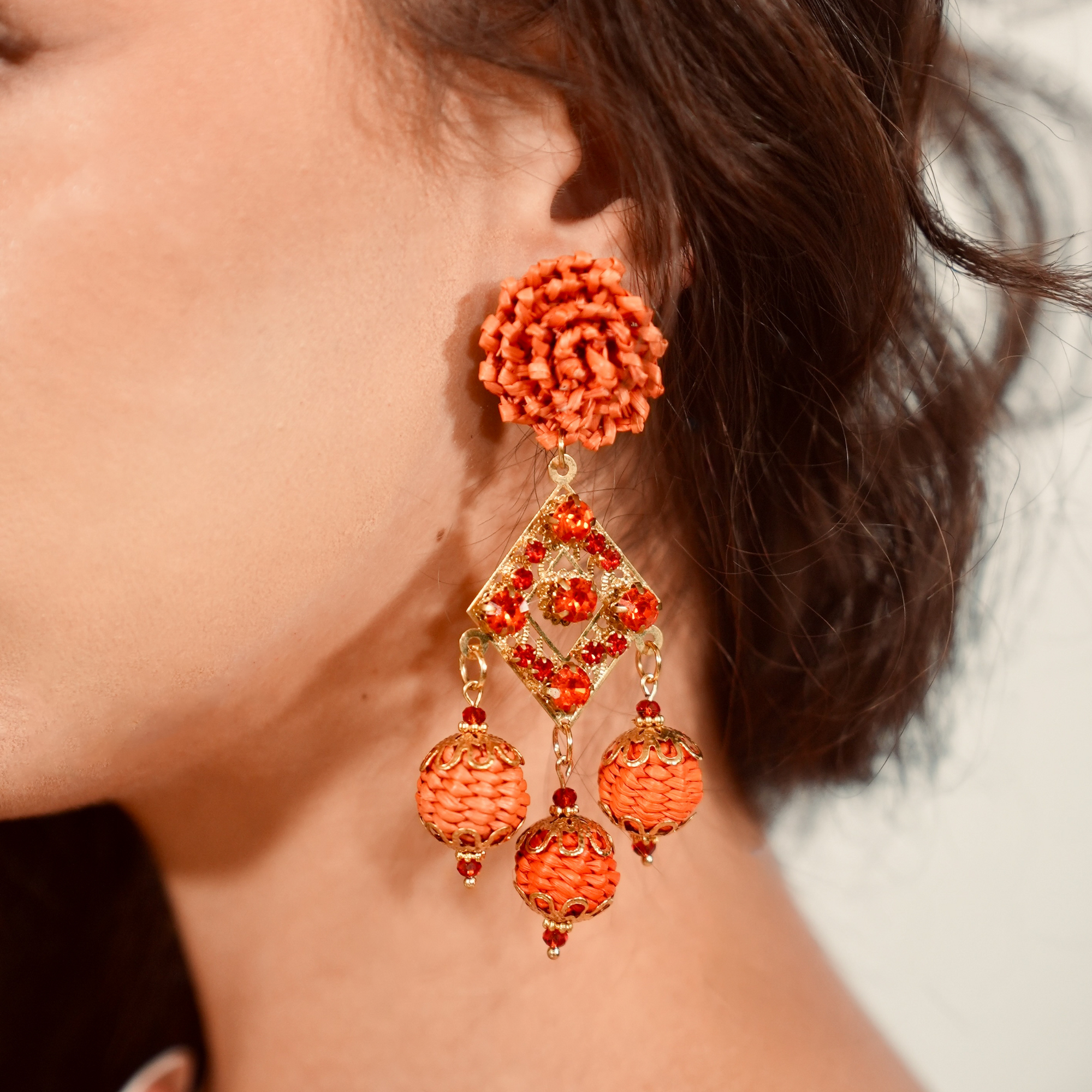 Close-up of a person wearing orange floral earrings with gold accents.