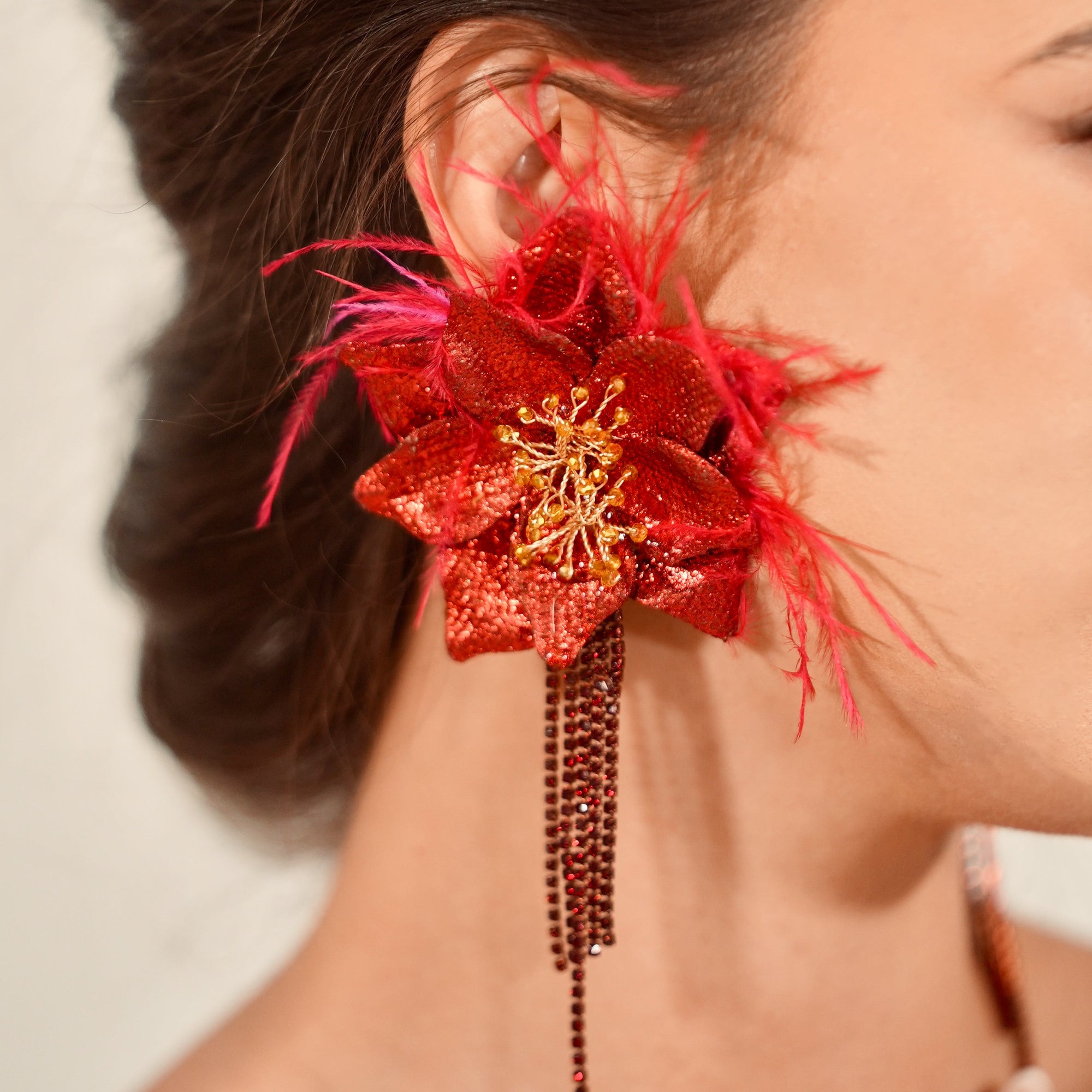 Close-up of a person wearing a red floral earring with feathers and beads.