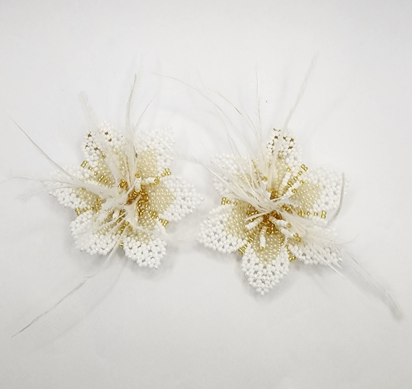 Handcrafted floral earrings with intricate white and gold beadwork, accented by delicate feathers.