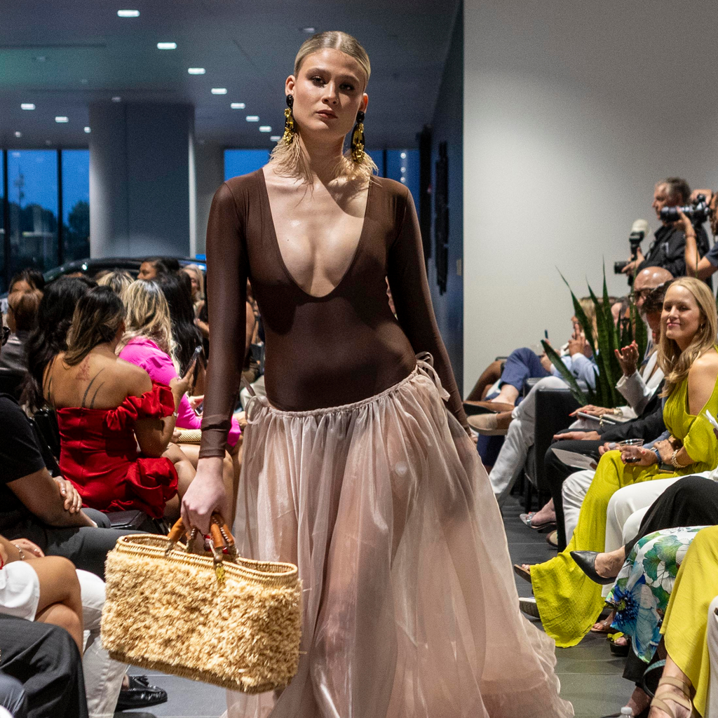 Fashion model holding Iraka Leather Beach Bag on the runway, wearing a brown bodysuit and blush tulle skirt
