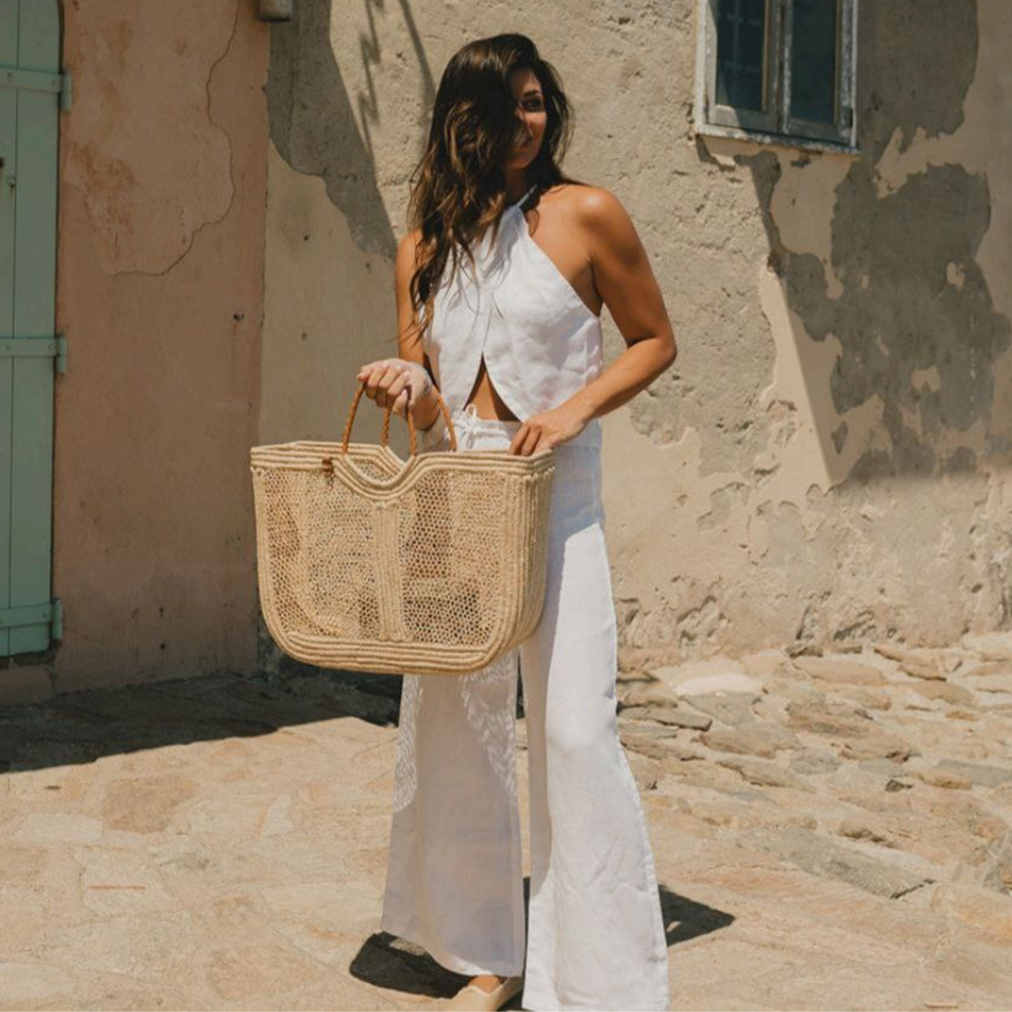 Woman holding Enea Leather Beach Bag while wearing white outfit, styled for summer