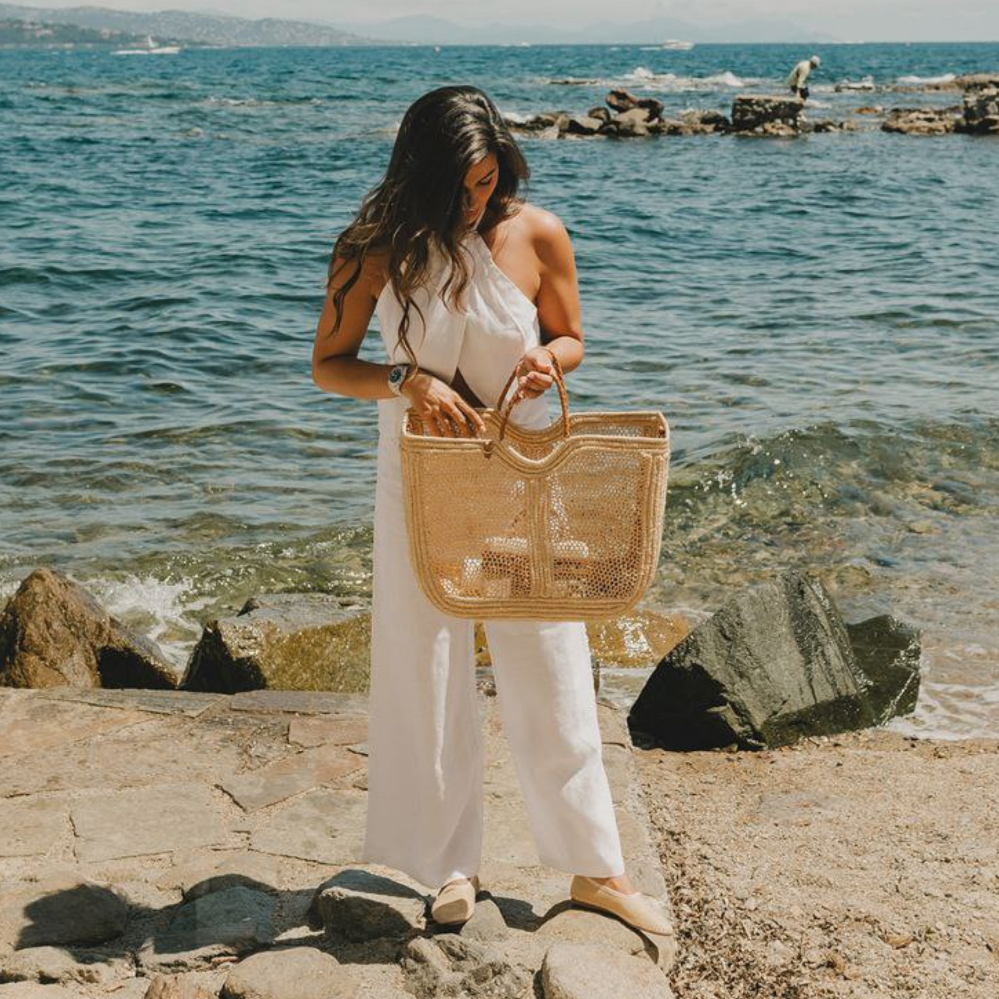 Woman at the beach holding the Enea Leather Beach Bag in a coastal setting