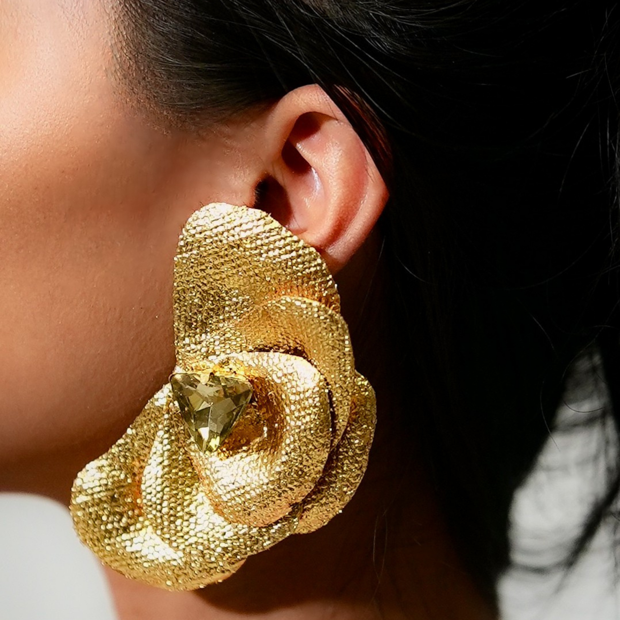 Gold floral earring worn by a person with a blurred background