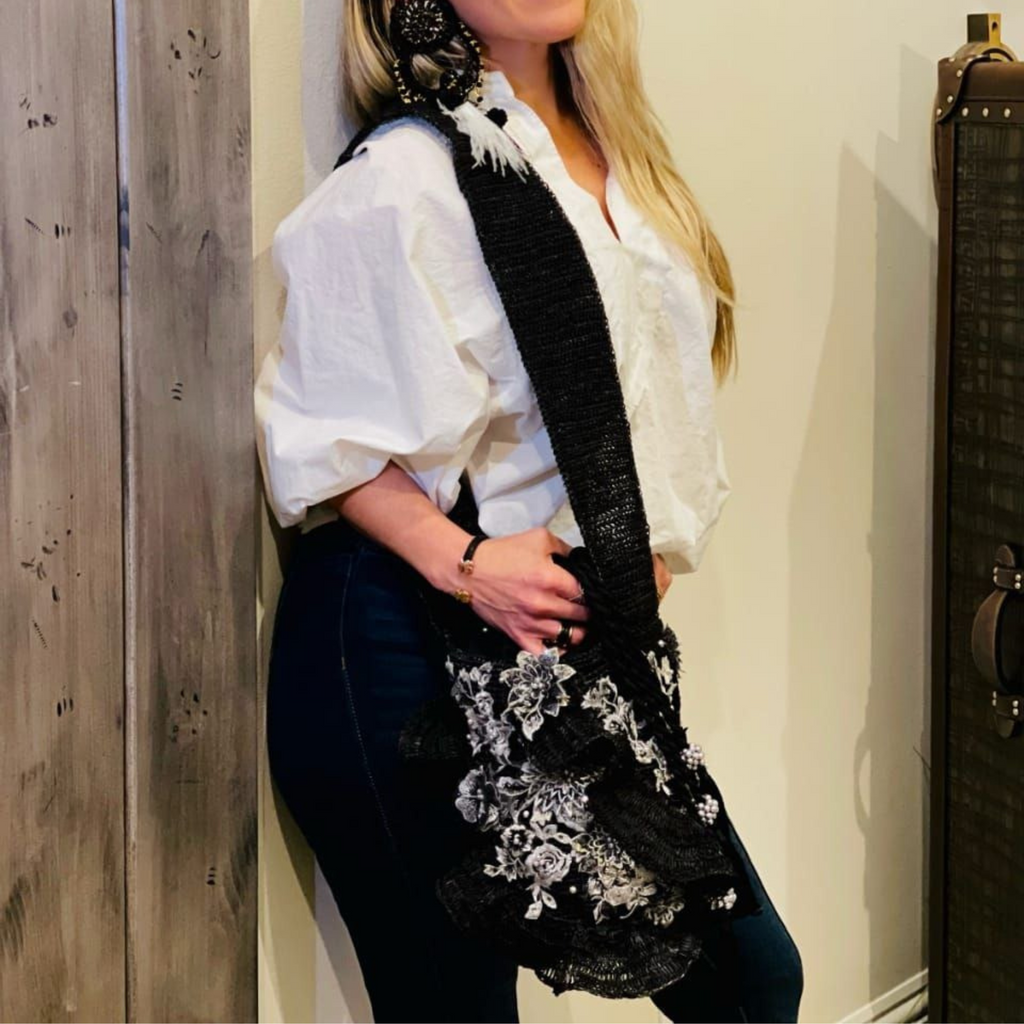 Woman wearing a handcrafted black shoulder bag with floral embroidery, styled with a white blouse and dark jeans.