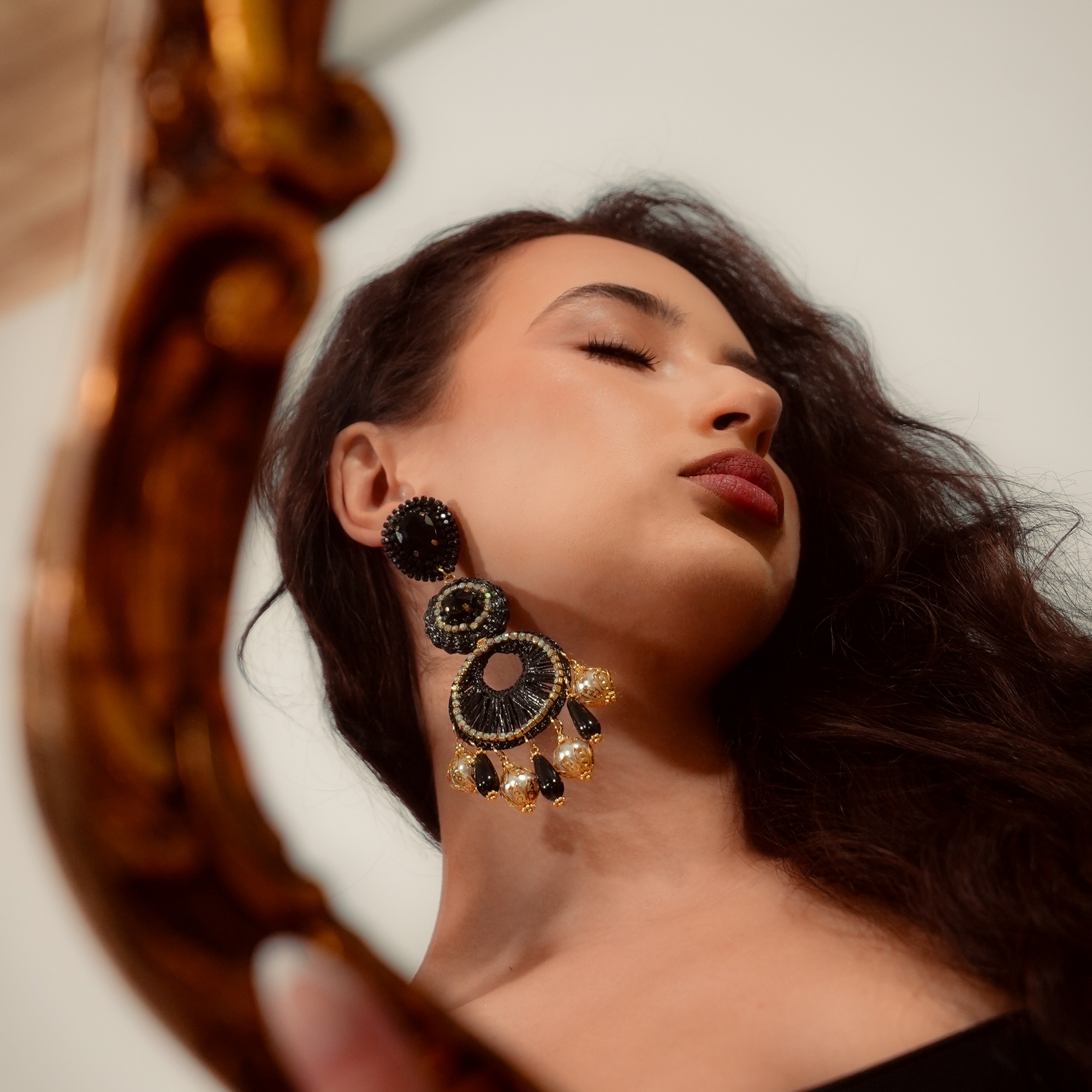 Woman wearing large, ornate earrings with a decorative mirror in the foreground
