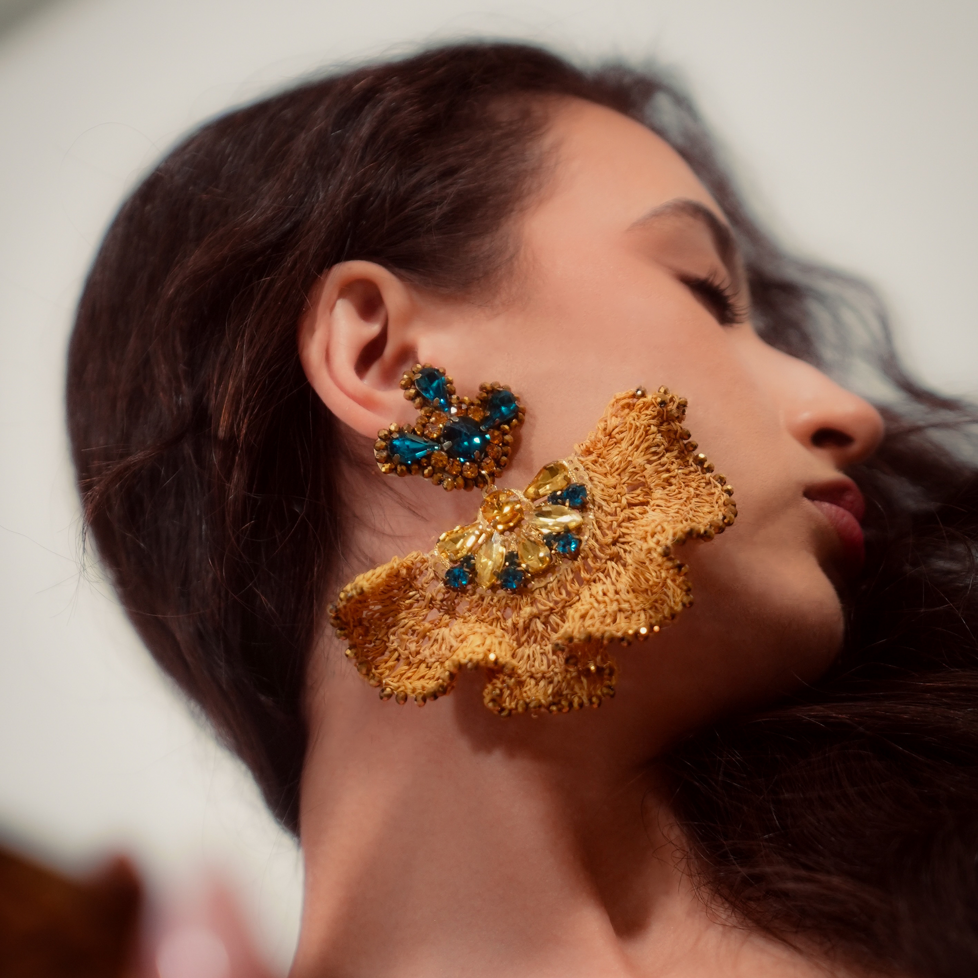 Close-up of a woman wearing gold earrings with blue gemstones on a neutral background