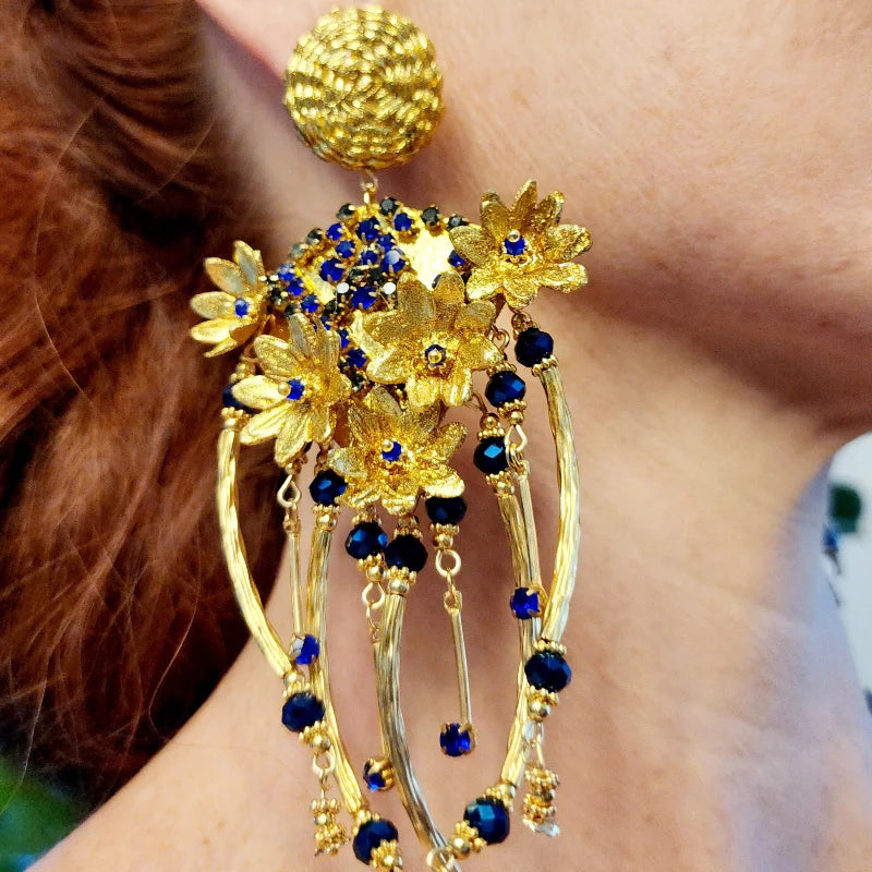 Close-up of a woman wearing an ornate gold and blue earring against a neutral background
