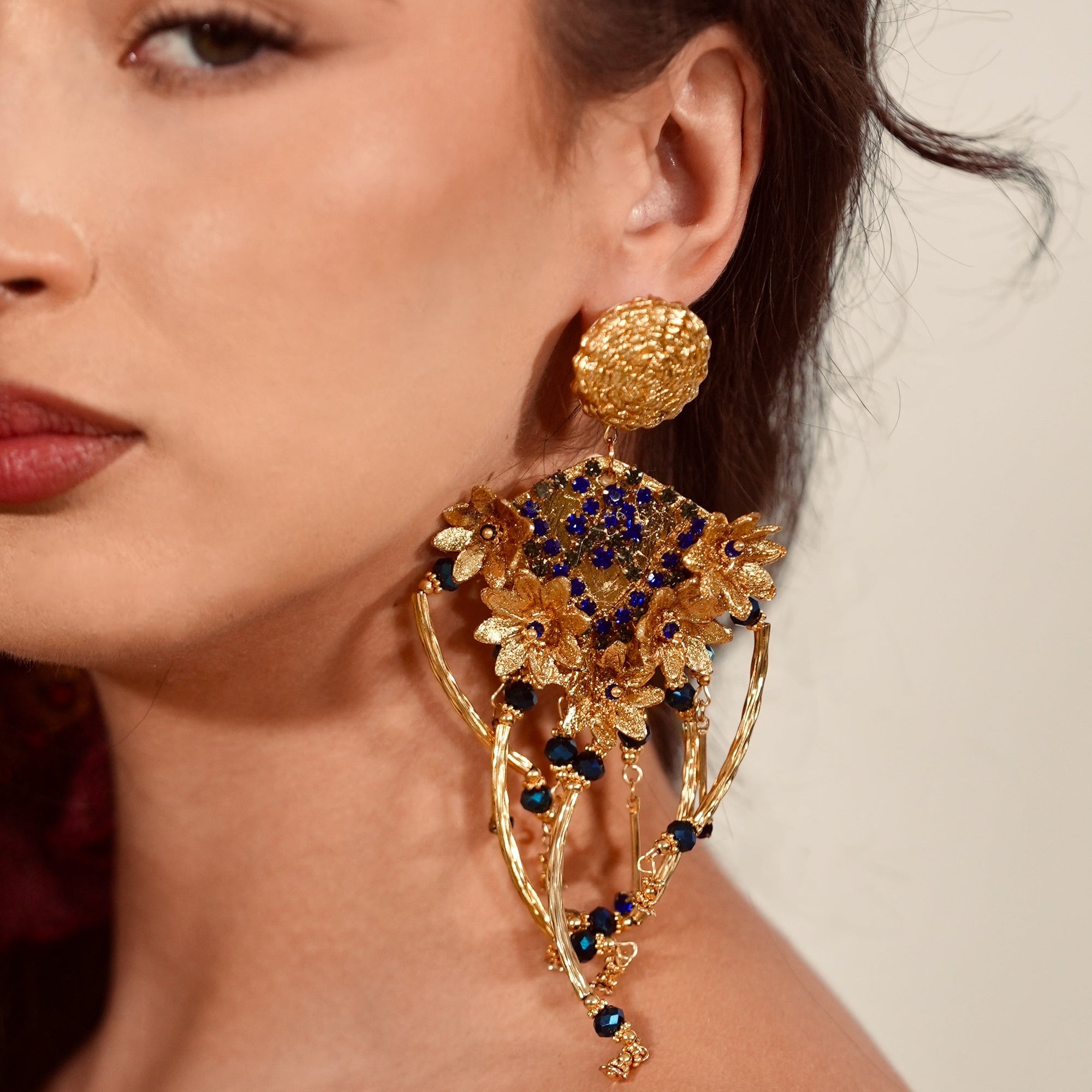 Close-up of a woman wearing an ornate gold and blue earring against a neutral background