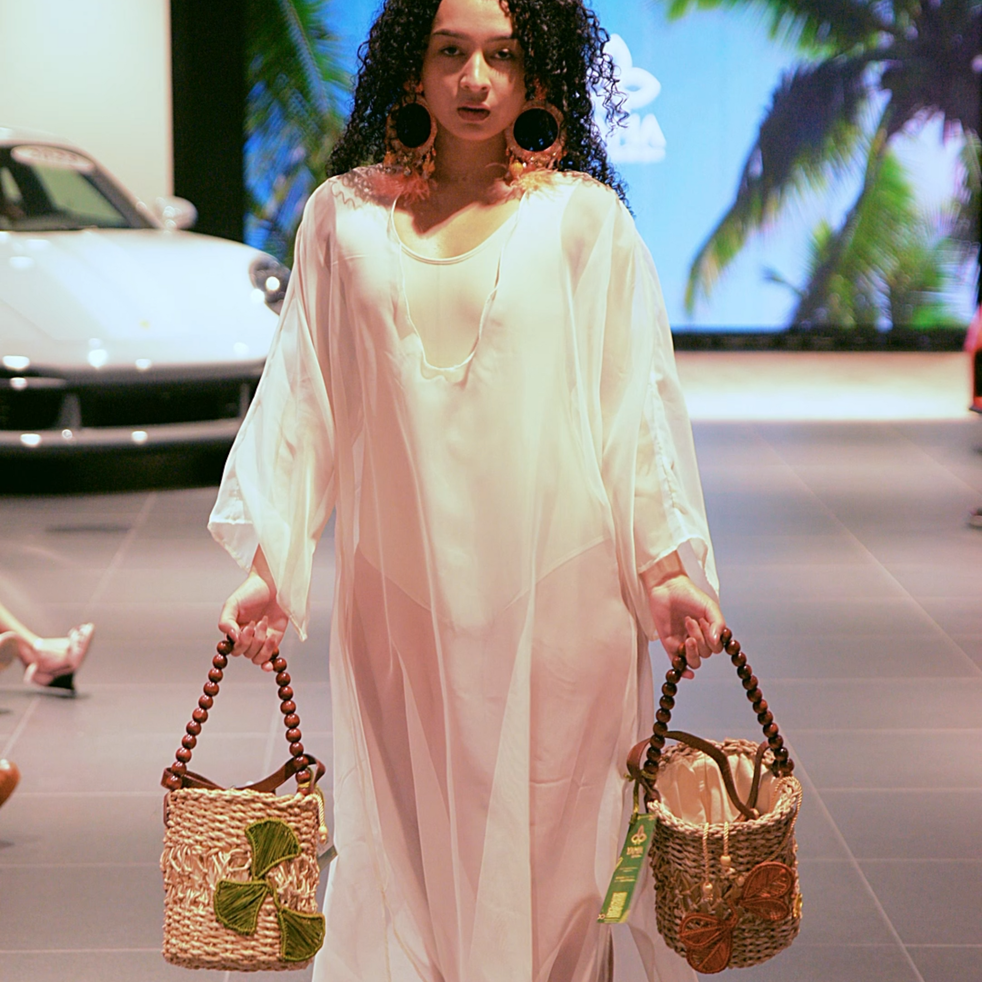 Model on the runway holding two Bucket Flower Bags with green and orange flower accents and wooden handles