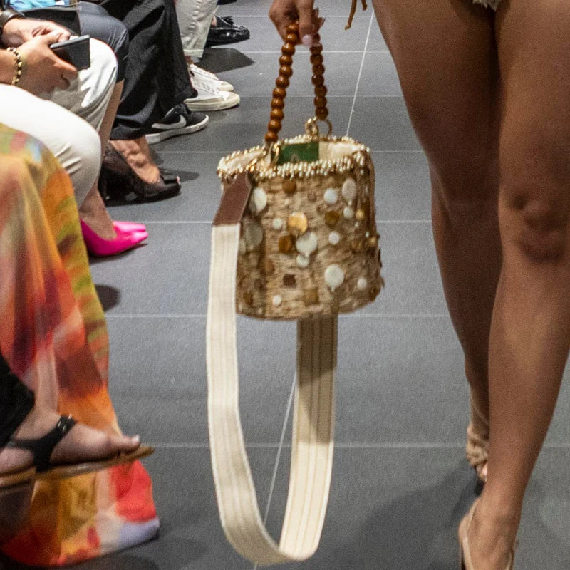 Model holding the Pearl Coral Bag on a runway, highlighting the pearl and shell embellishments and wooden handle.