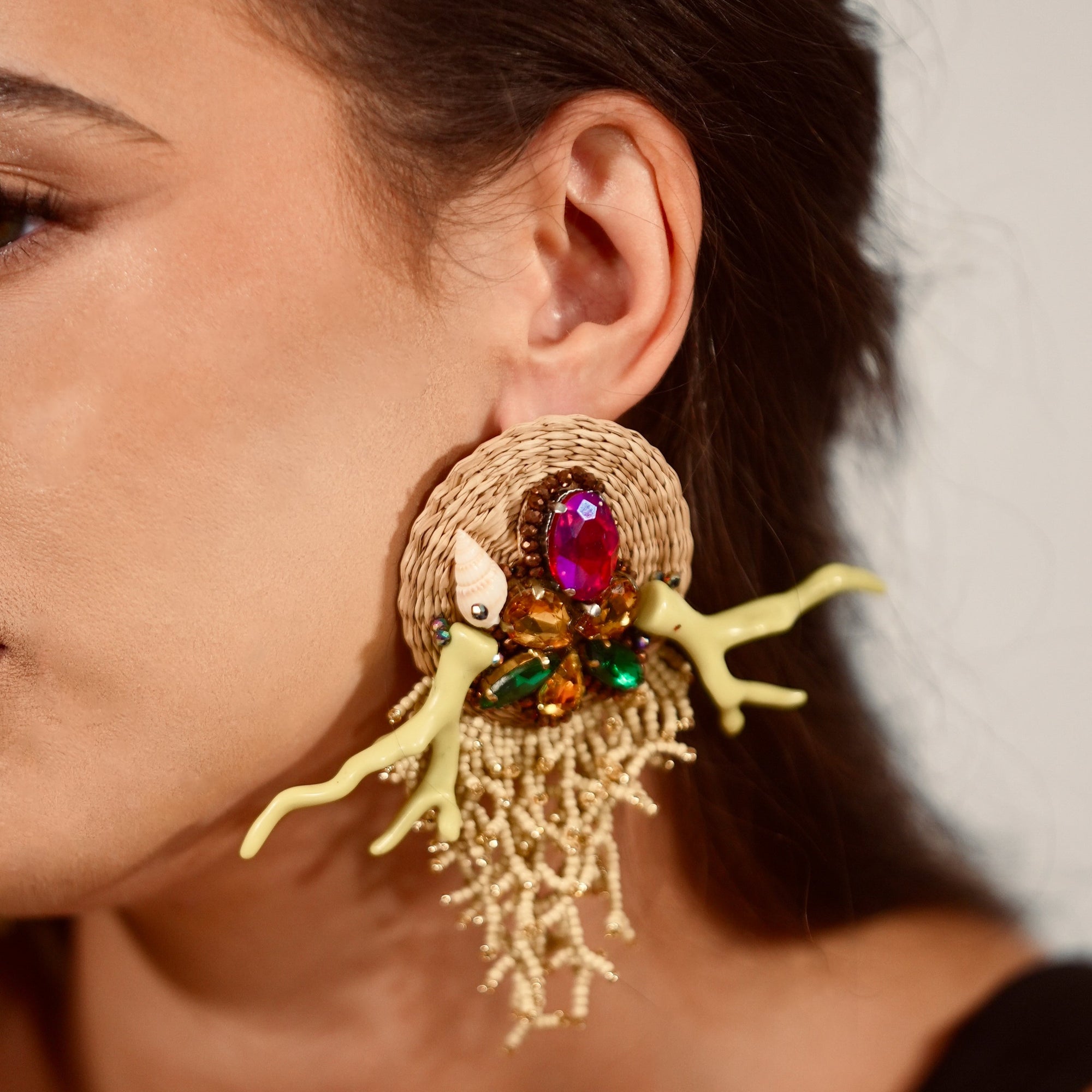 Close-up of a woman wearing a large, colorful earring with a gemstone.