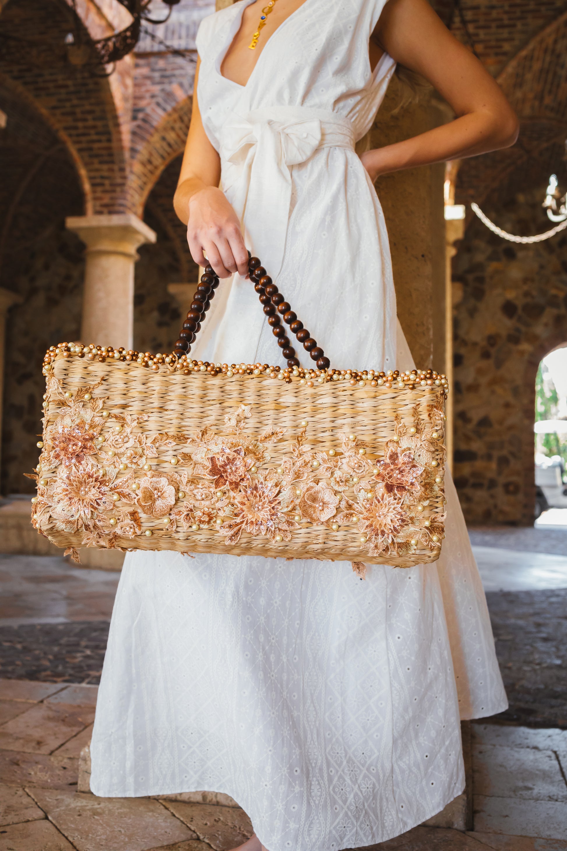 Rectangular wicker handbag with floral appliqués, pearl accents, and banana wood handles.