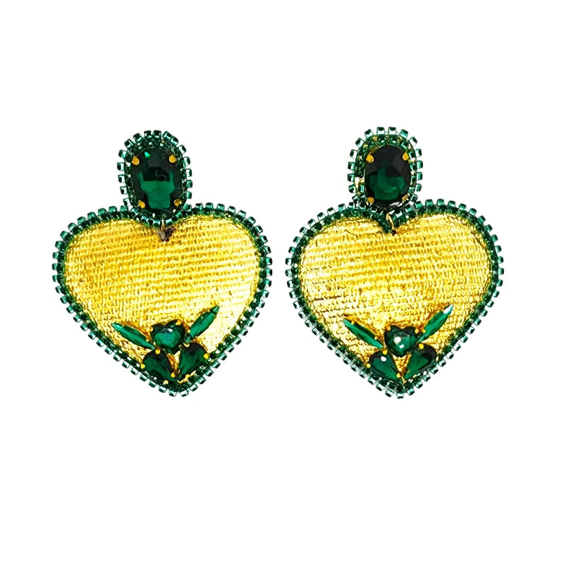 Bold and elegant earrings featuring a golden heart shape adorned with green gemstones. The intricate design includes a decorative frame of green beads and additional stones at the heart's center, making them a stunning accessory for any occasion.