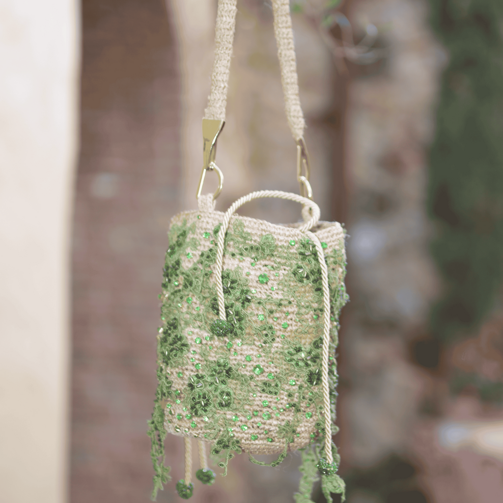 Artisanal crossbody bag with green embroidered details and natural fiber strap, hanging outdoors