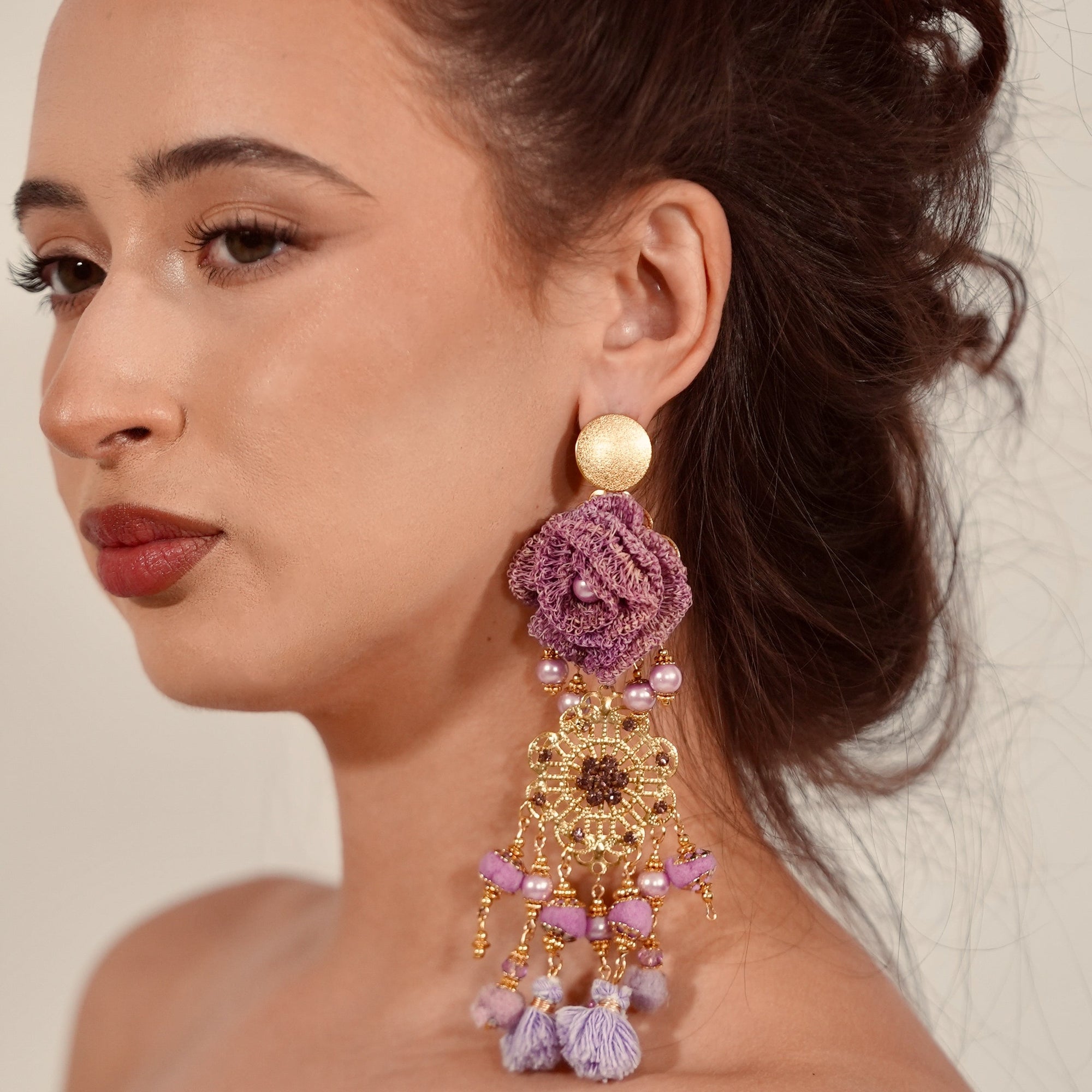 Woman wearing a large, ornate earring with floral design and gold accents.