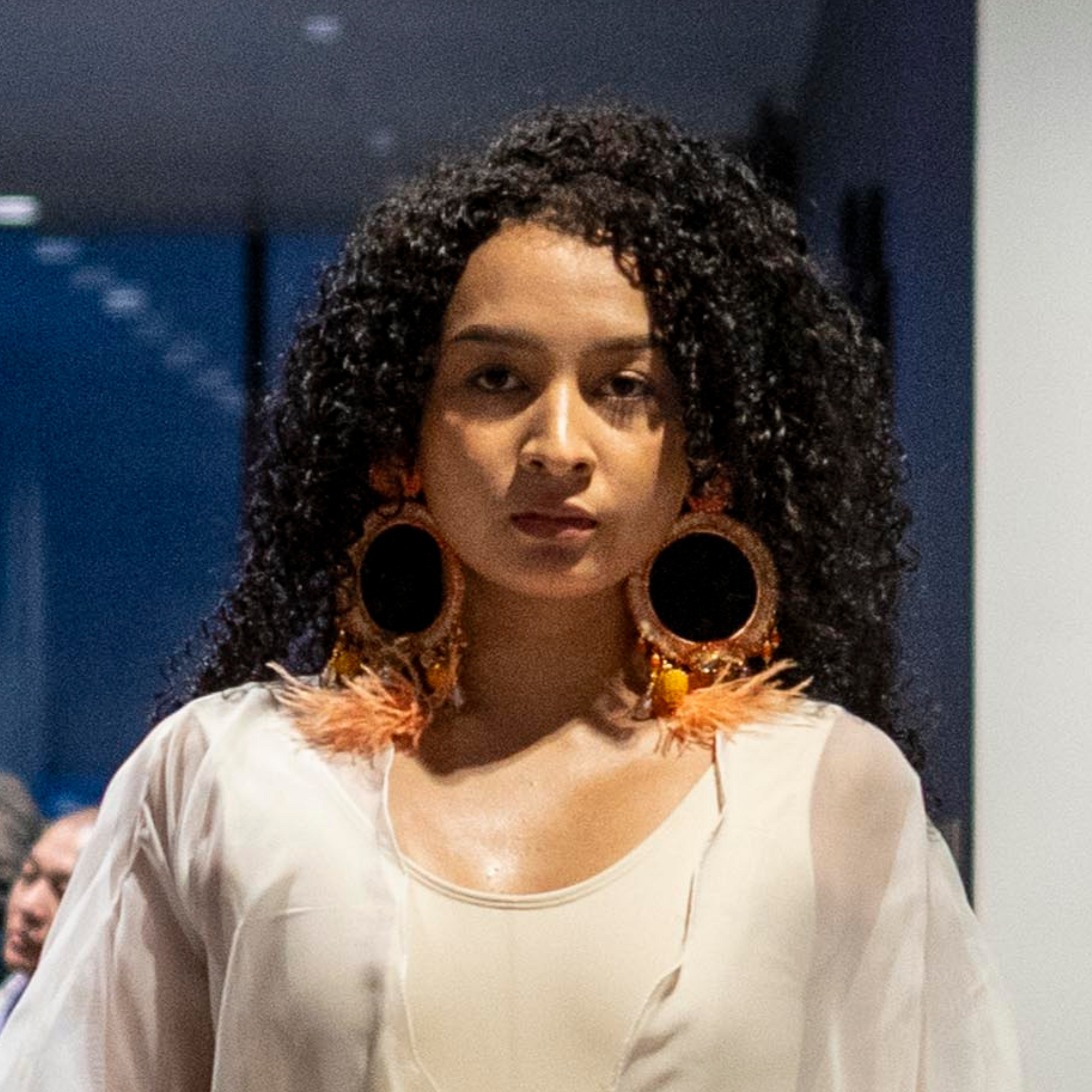 Model wearing Feather Whole Moon Earrings with banana fiber embroidery, gemstone accents, and soft peach feathers — handcrafted Colombian jewelry