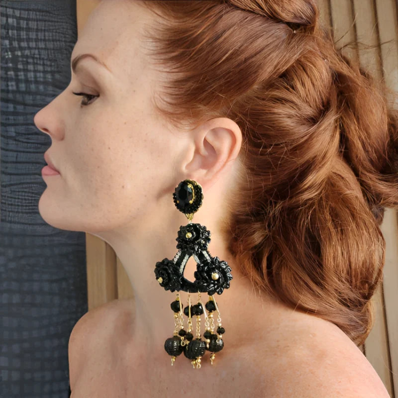 A person wearing a black and gold fiber oval flower earring with day and night design.