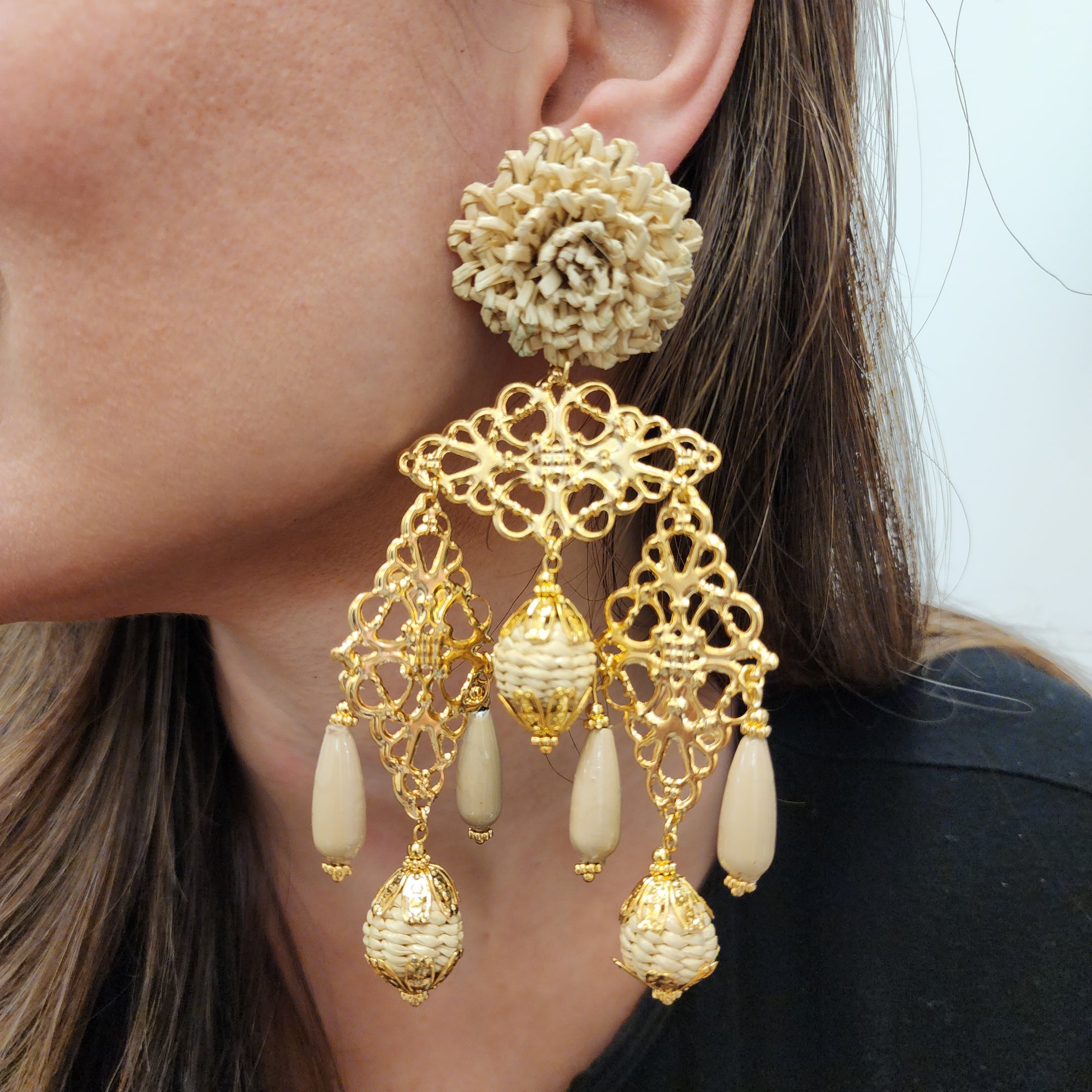 Side profile of a woman wearing beige and gold statement earrings with intricate textures and golden accents.