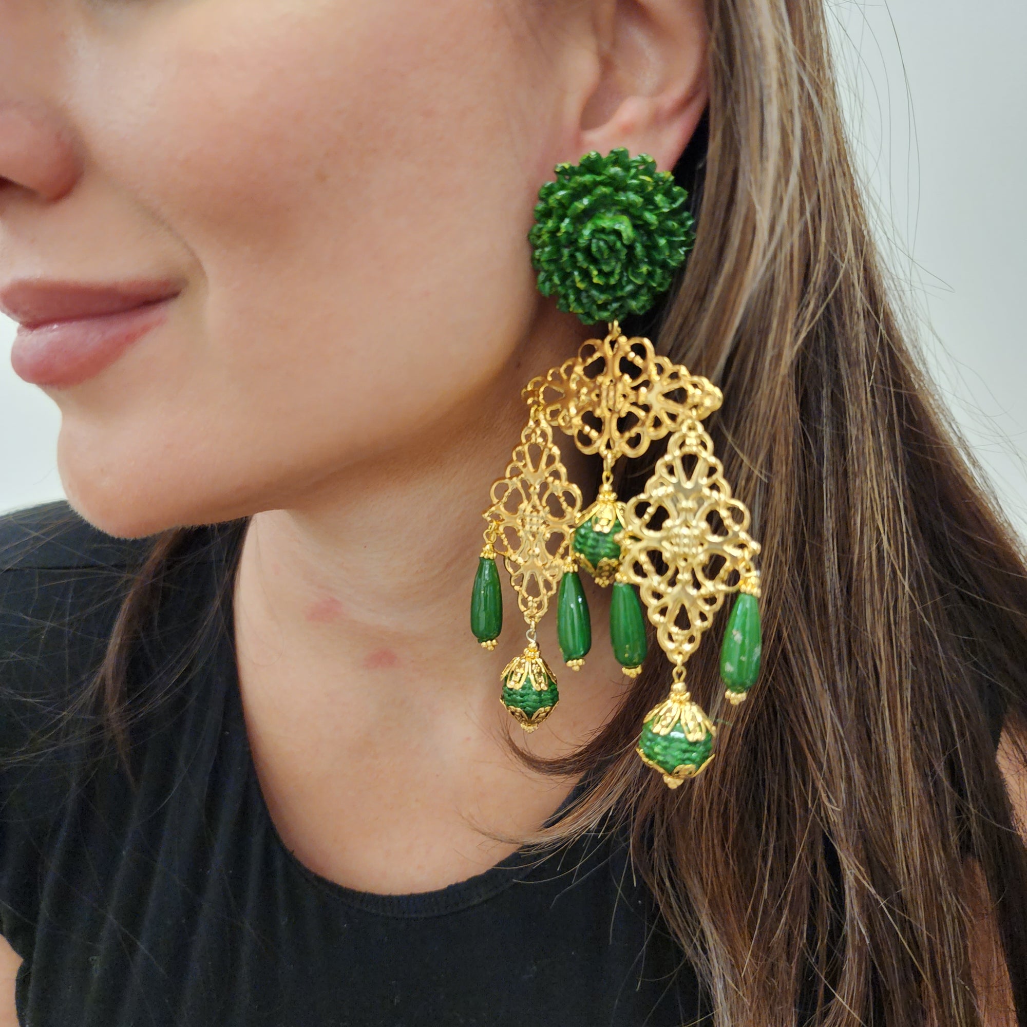 Close-up of a woman wearing handcrafted green and gold earrings with floral top and filigree drops.