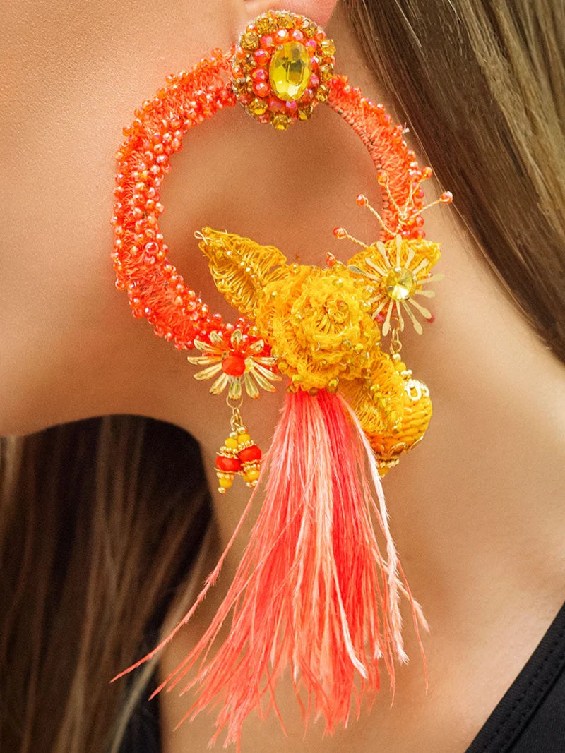 Handcrafted earrings made by Colombian artisans in the shape of a new moon, embroidered with banana fiber and featuring a banana fiber flower at the top. Adorned with gemstones or painted banana fiber embroidery, they may also come with feathers and are available in various colors.