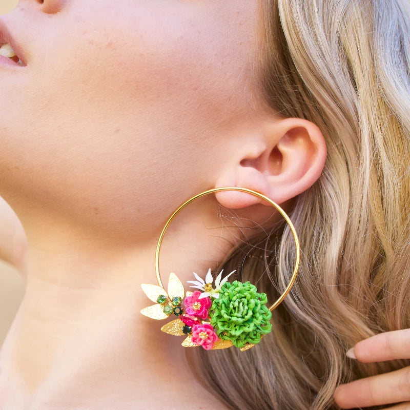 These stunning golden earrings feature delicate handcrafted flowers made from banana fiber, painted in vibrant green, white, and fuchsia