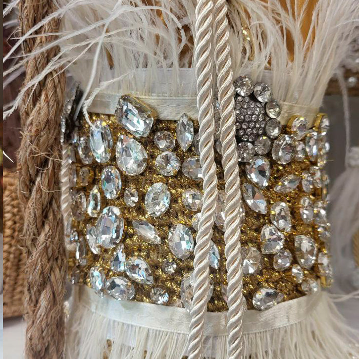 Close-up of gold and silver bucket bag with white feathers and crystal embellishments, showing the rope strap detail.