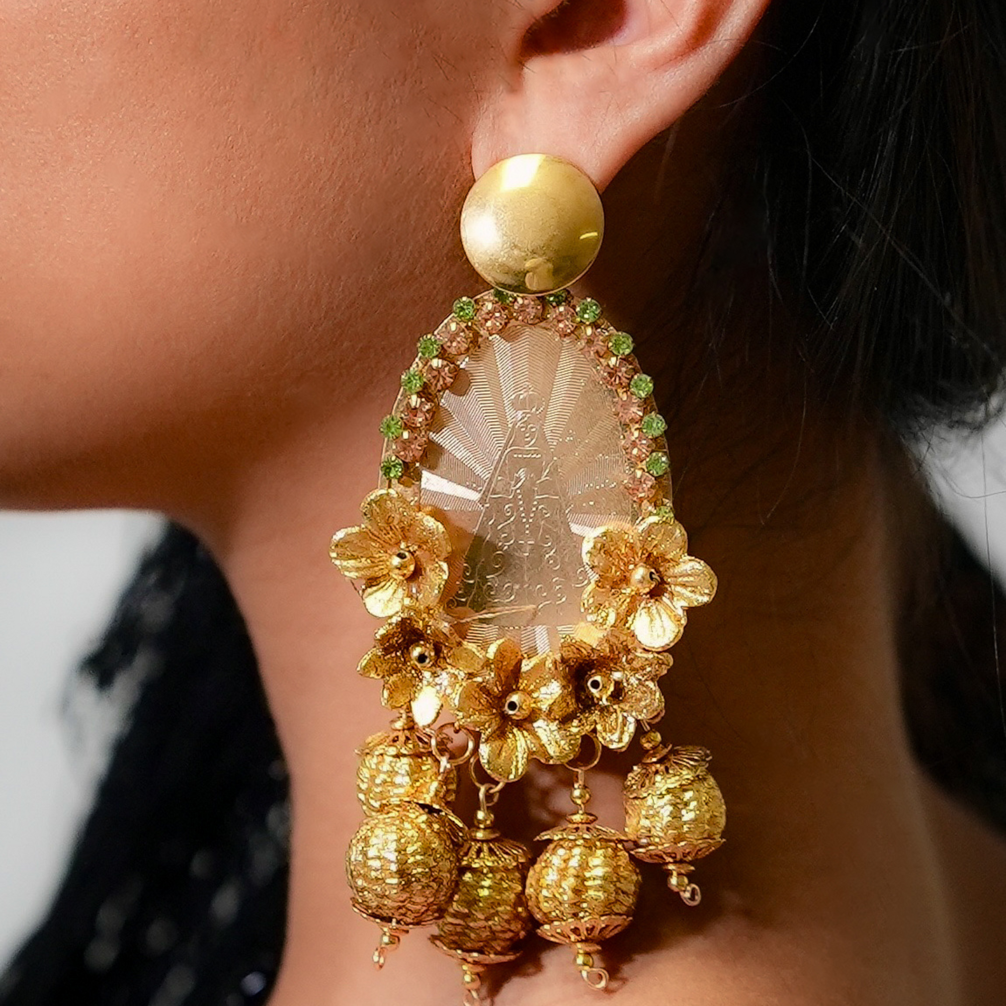 Gold earrings with floral designs and a clear central stone worn by a person.