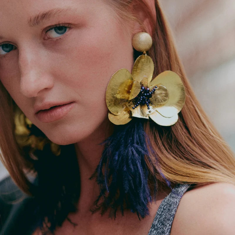 These handmade earrings crafted by Colombian artisans feature banana fiber material painted in gold and adorned with purple feathers.