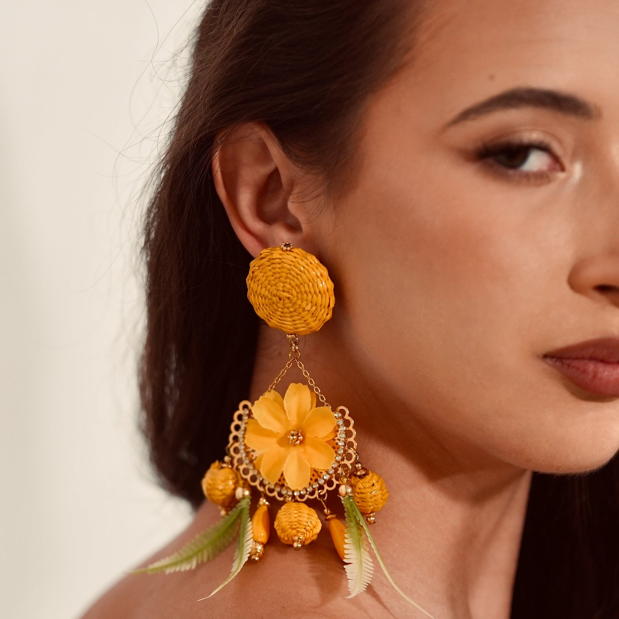 Woman wearing a pair of yellow floral earrings against a neutral background