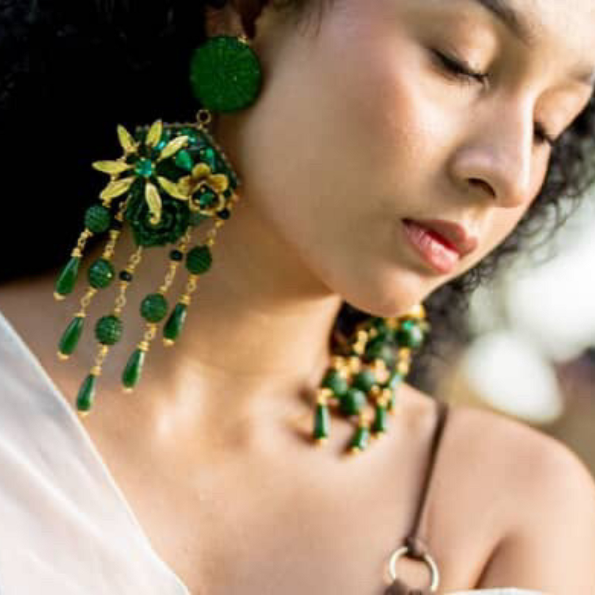 Woman wearing vibrant green and gold floral earrings with dangling elements, styled in a soft, natural outdoor setting.