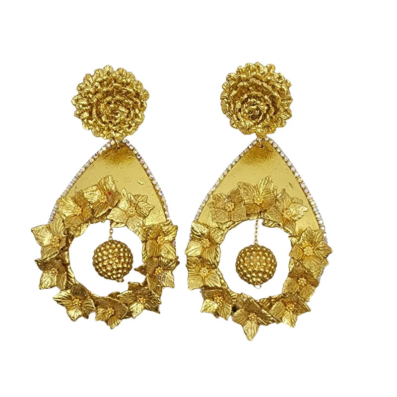 Handcrafted by Colombian artisans, these earrings feature two types of banana fiber flowers painted in gold, adorned with clear gemstones, and shaped like totumo material leaves. A hanging sphere made from gold-painted banana fiber sits at the center, adding elegance and sophistication to this unique design.
