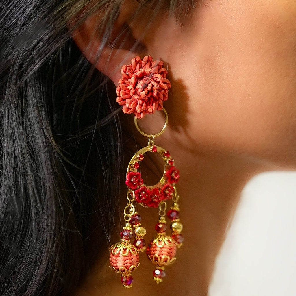Close-up of a person wearing red floral earrings with gold accents.