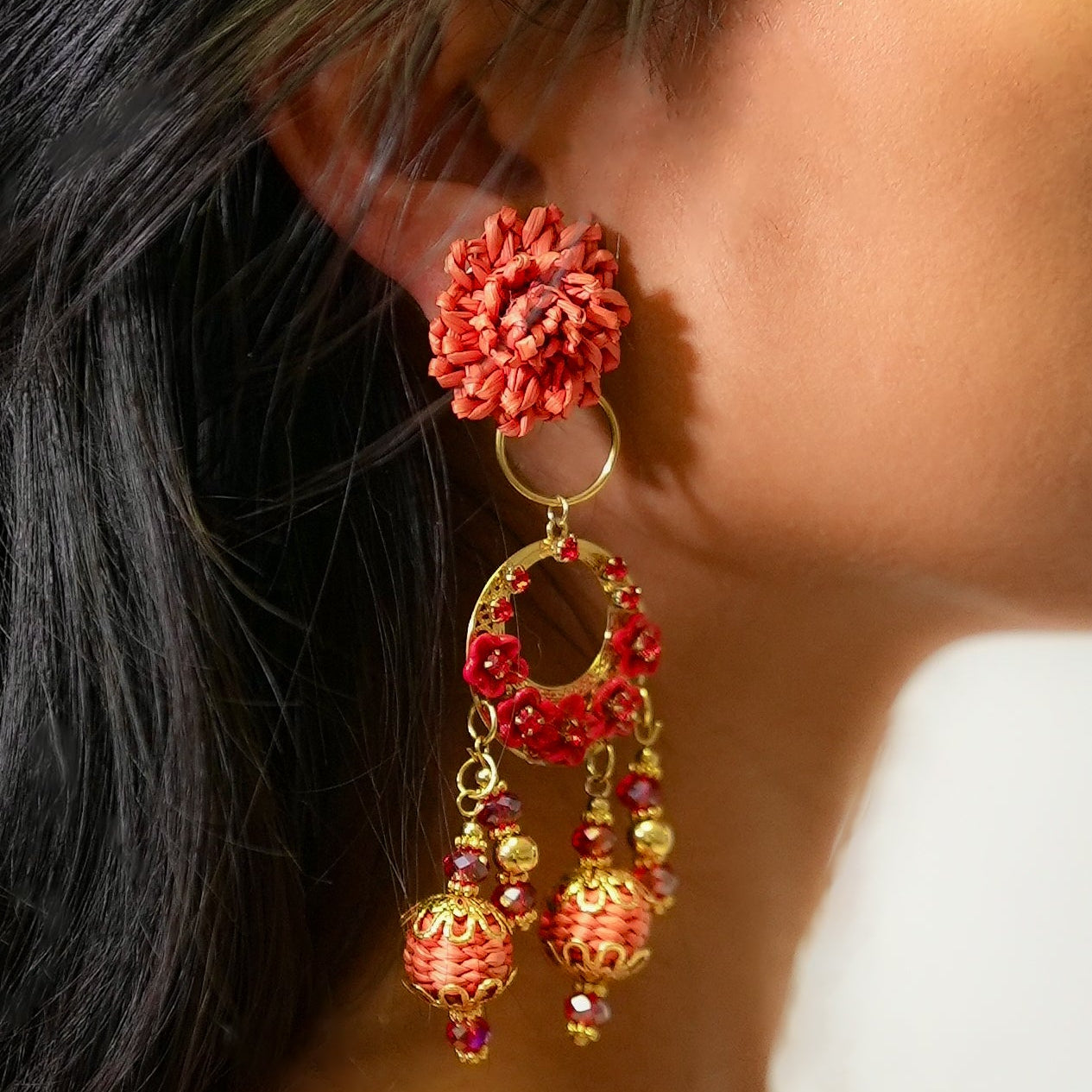 Close-up of a person wearing red floral earrings with gold accents.