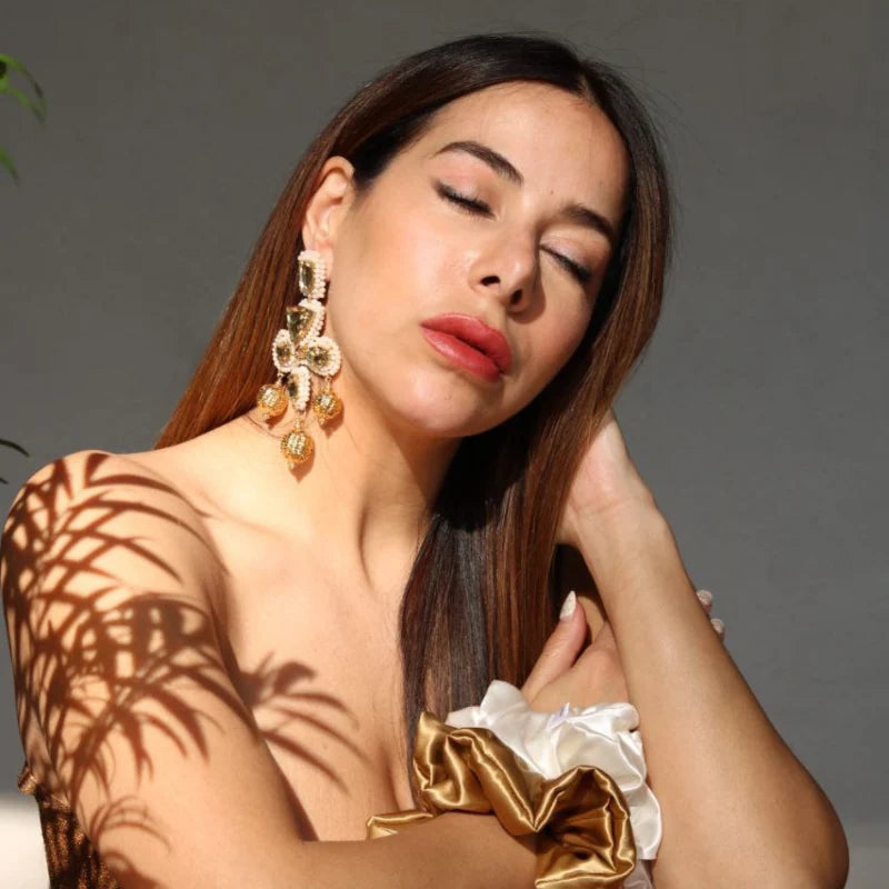 These handcrafted earrings blend artisanal mastery with timeless charm, featuring intricate beadwork and golden accents. The dangling golden orbs add a dynamic touch, exuding opulence and purity.