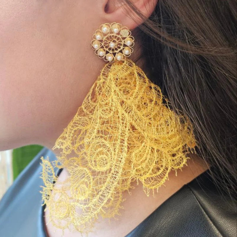 Close-up of a person wearing a gold earring with yellow lace detail.