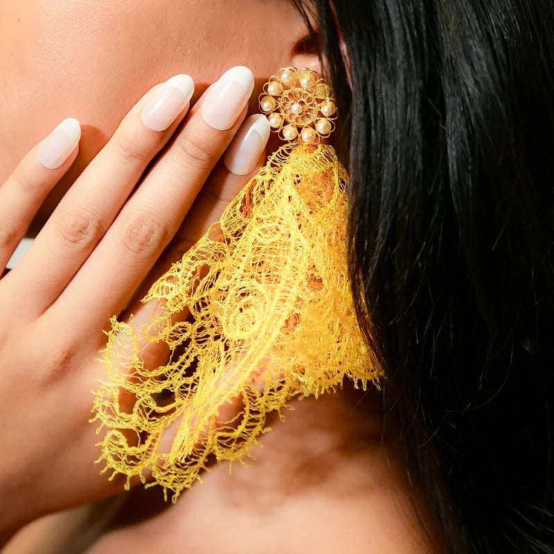 Close-up of a person wearing a gold earring with yellow lace detail.