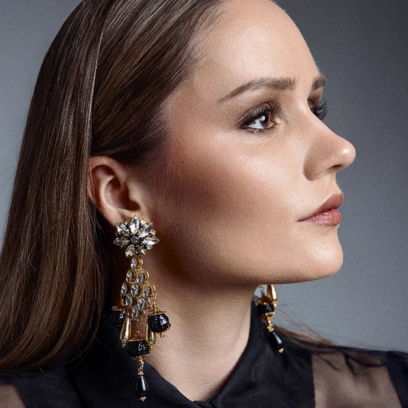 These earrings feature transparent and black gemstones at the top, cascading down with golden sheets decorated with touches of transparent gemstones.