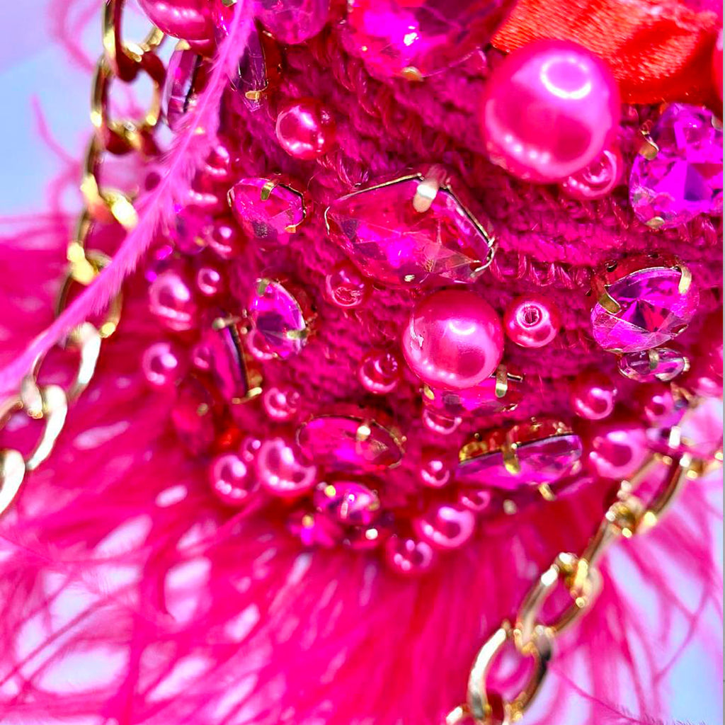 Close-up of the fuchsia feather minaudière showing pink gemstones and gold chain.