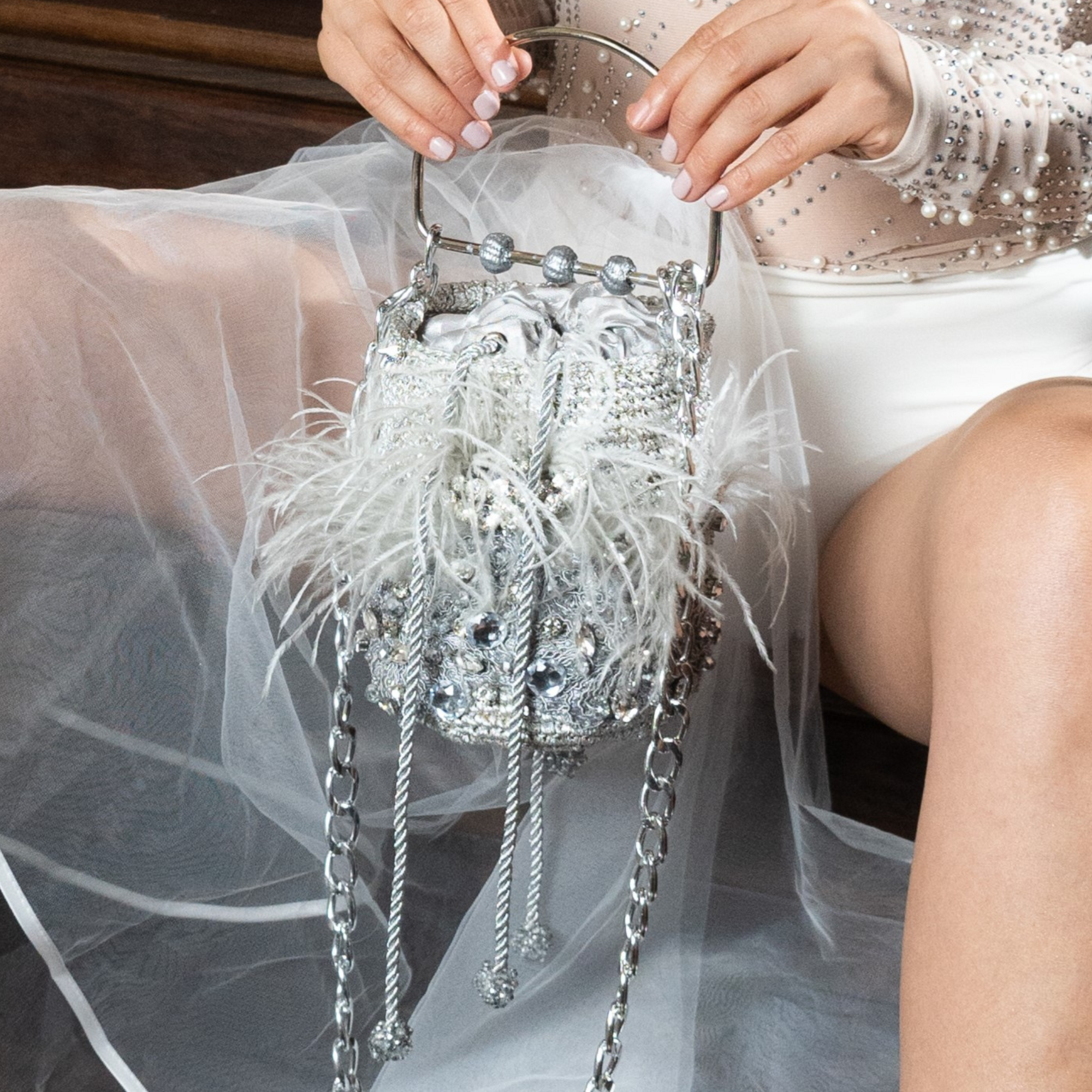 Minaudière Silver & Feather Bag resting on model’s lap, showing ornate beading, chain accents, and elegant feathers