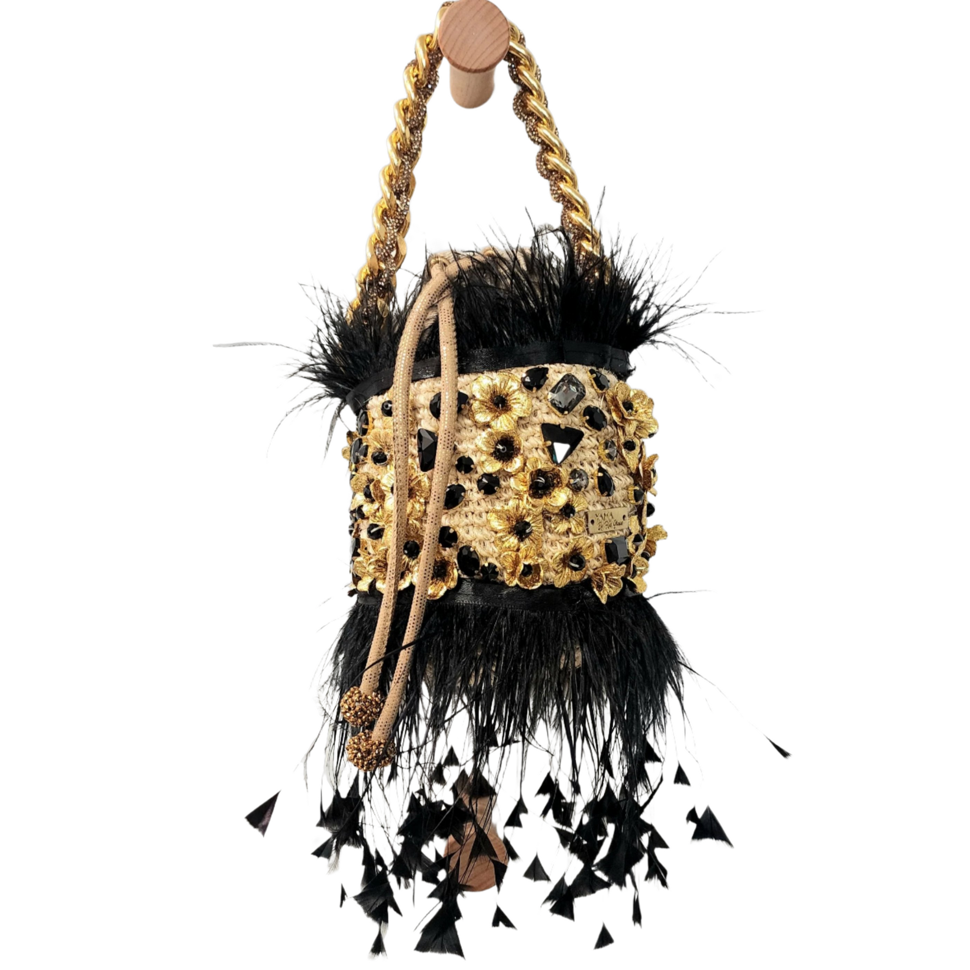 Handcrafted minaudiere bag with gold floral embroidery, black gems, and dramatic feather details, hanging from a wooden peg