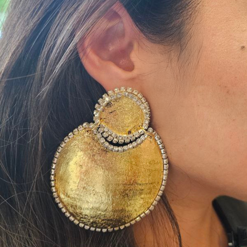 Close up of a person wearing large gold earrings with intricate designs.